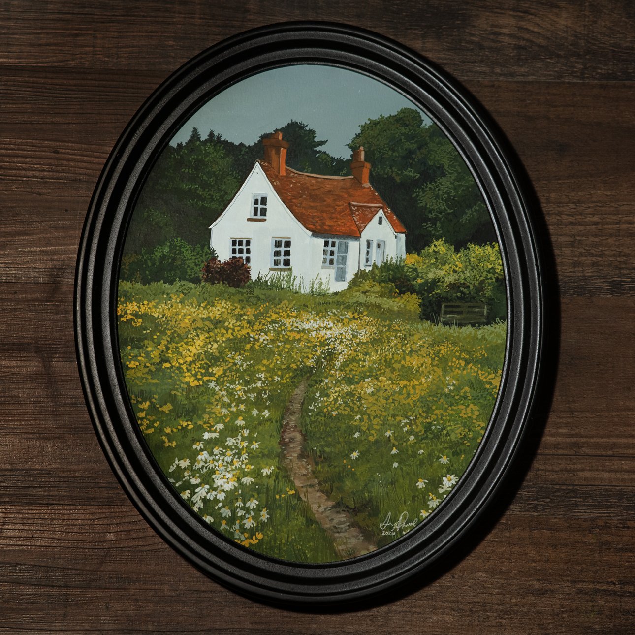 Painting of a white cottage with a red roof, surrounded by a field of yellow and white flowers, and trees in the background, framed in an oval black frame.