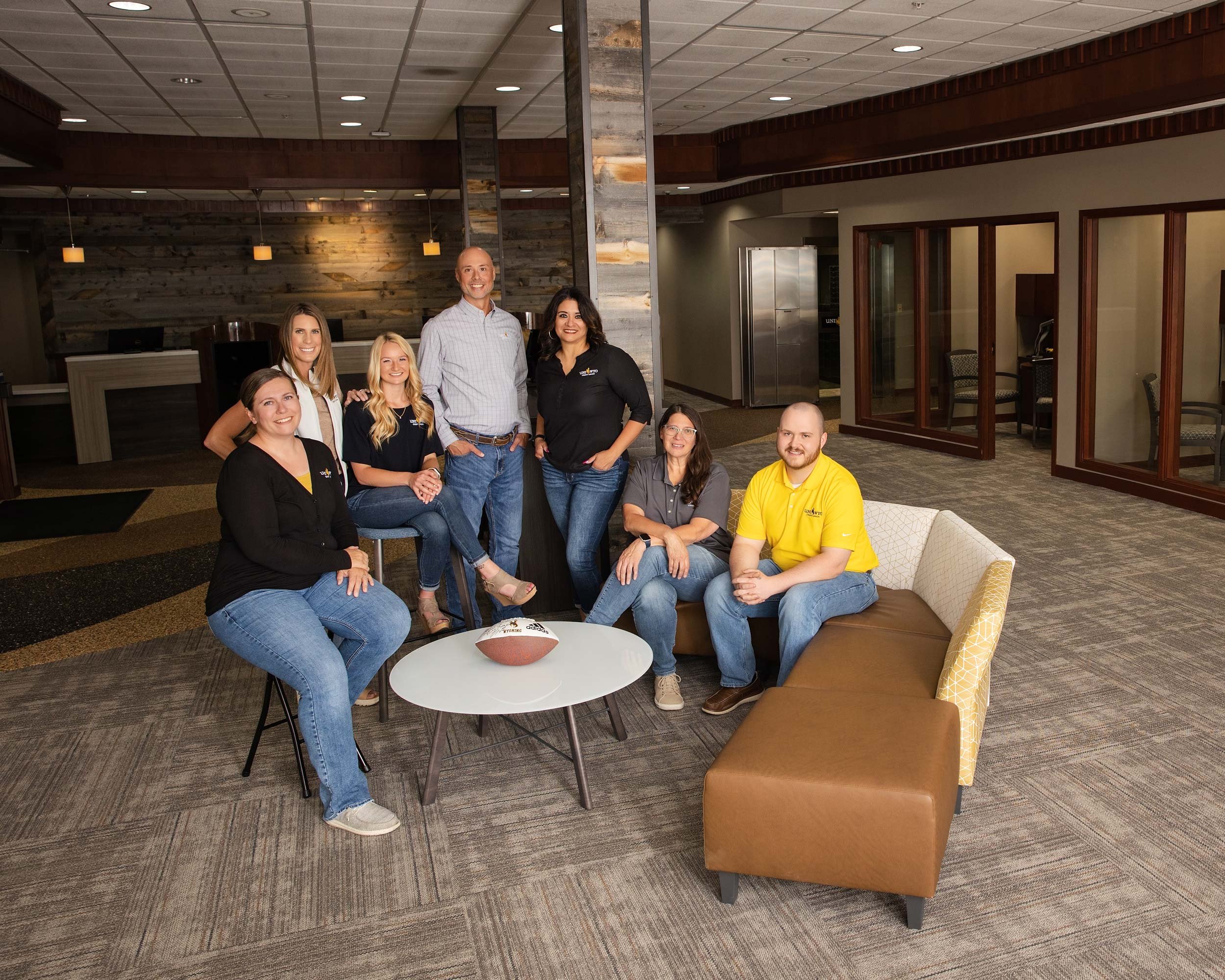UniWyo Credit Union team, group seated and standing around a table inside a branch office in Casper, Wyoming.
