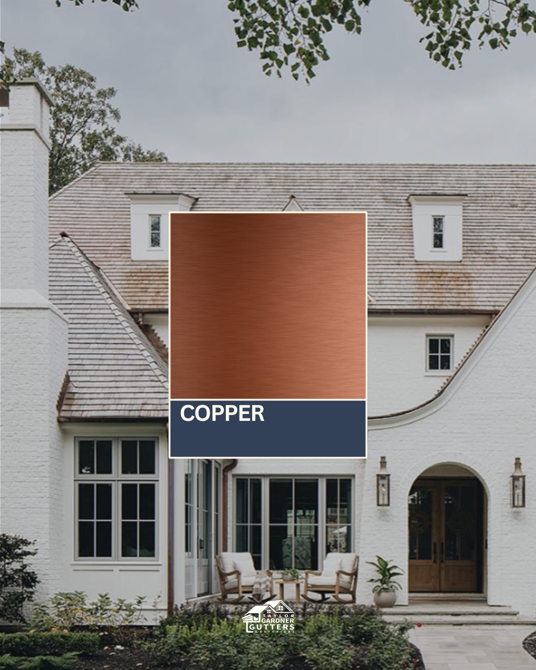 Exterior of a white house with a copper-colored roof and windows, outdoor seating area with chairs and a small table, garden with plants in front.