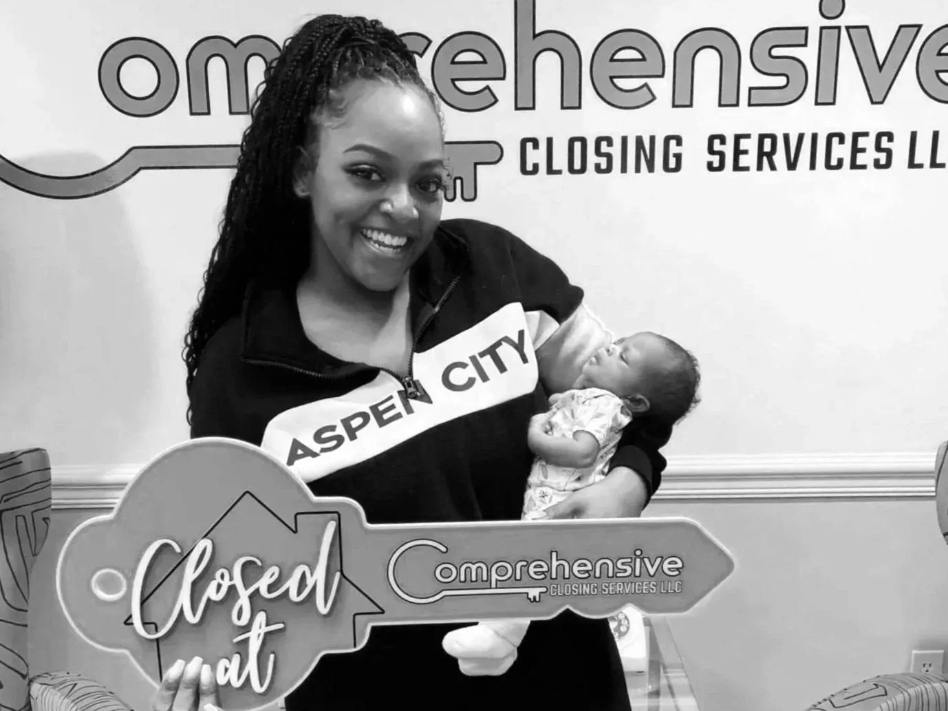 Young woman holding a newborn baby and a large key that says, 'Closed It' on it.