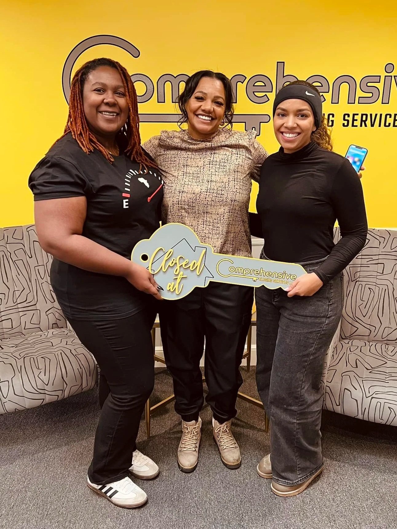 Three women smiling and holding a large key with 'Closed It' on it.
