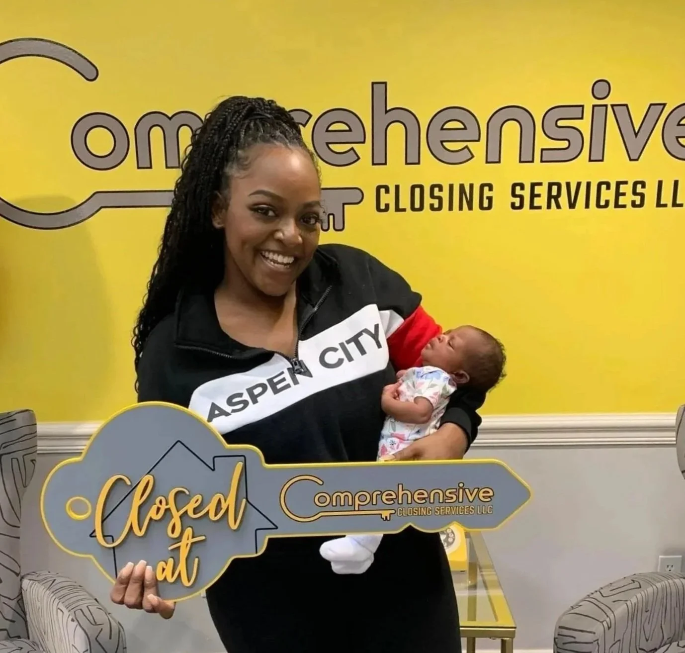 Young woman holding a newborn and a large key that says 'Closed It' on it.