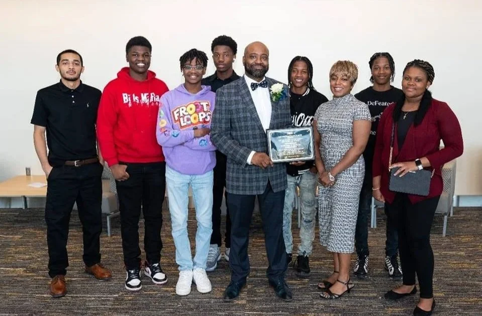 Group of teenagers with a man in the middle, holding a plaque, all smiling.