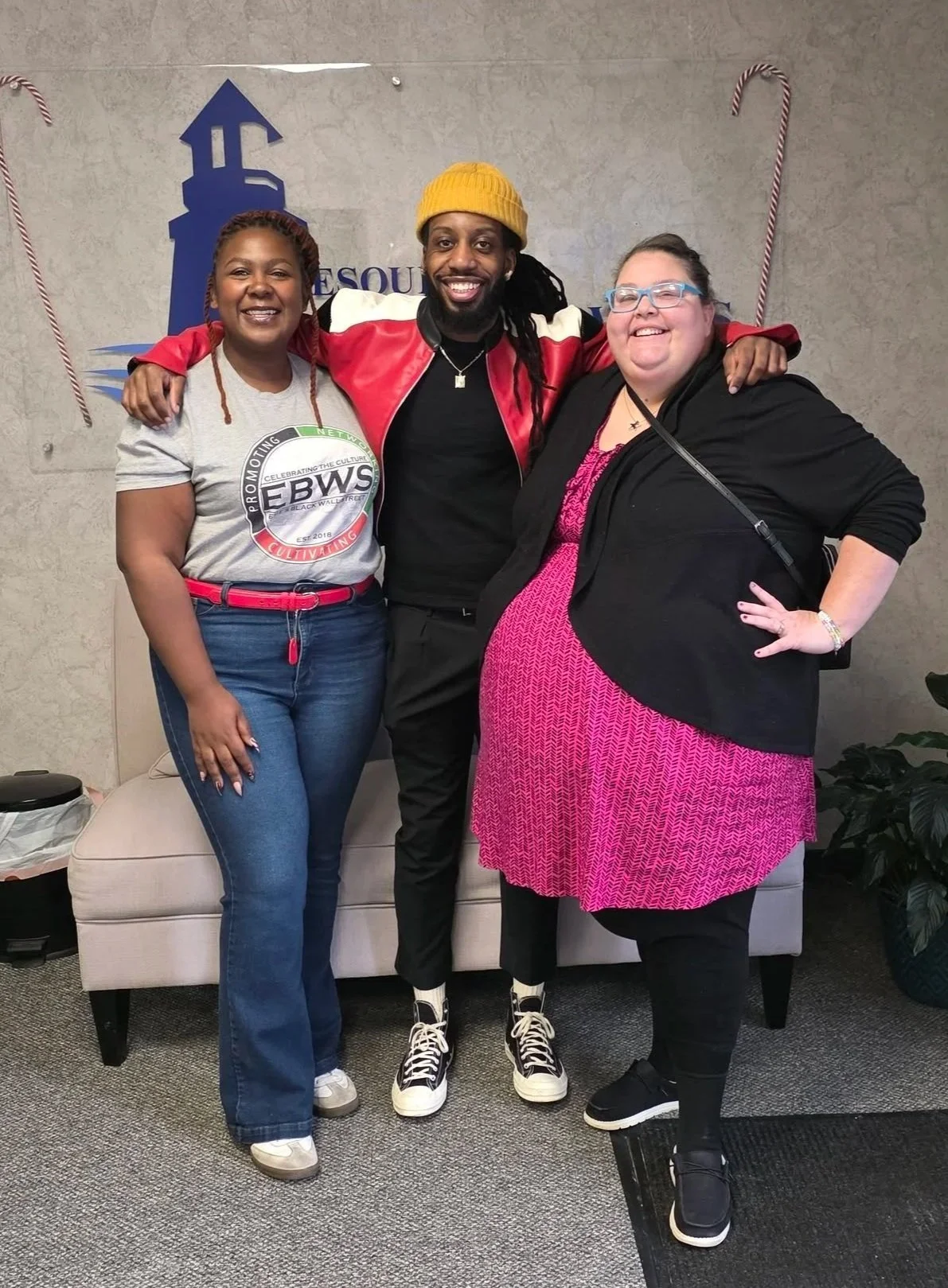 A man standing in between two women with his arms around their shoulders, all smiling.