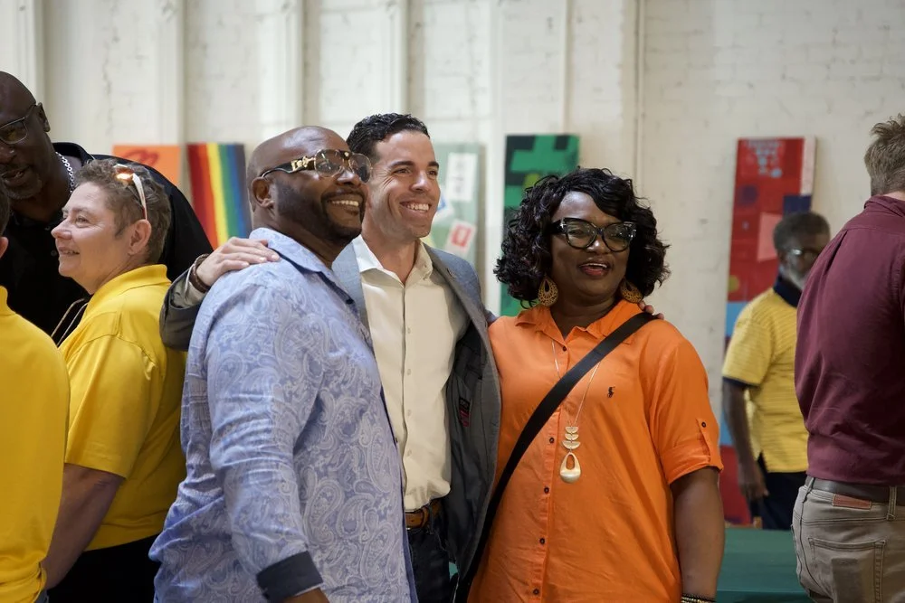Group of people smiling and posing for a photo in an indoor art gallery with colorful paintings in the background.