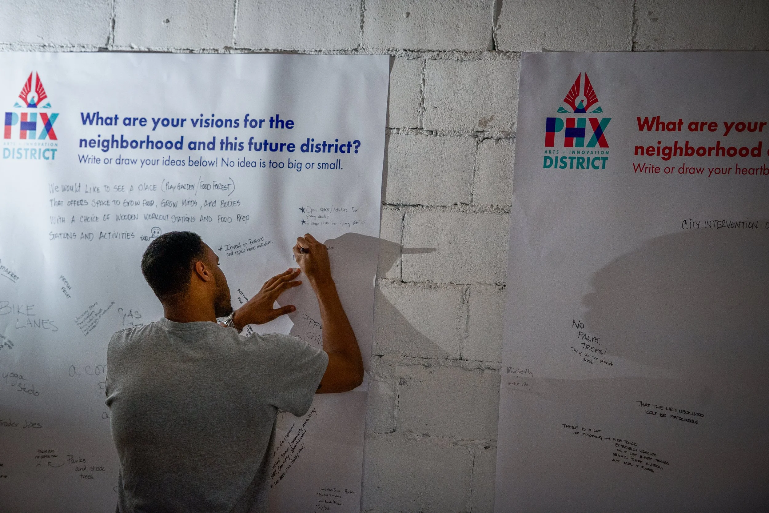Person writing ideas on a large poster board at a community event, with the poster titled "What are your visions for the neighborhood and this future district?"