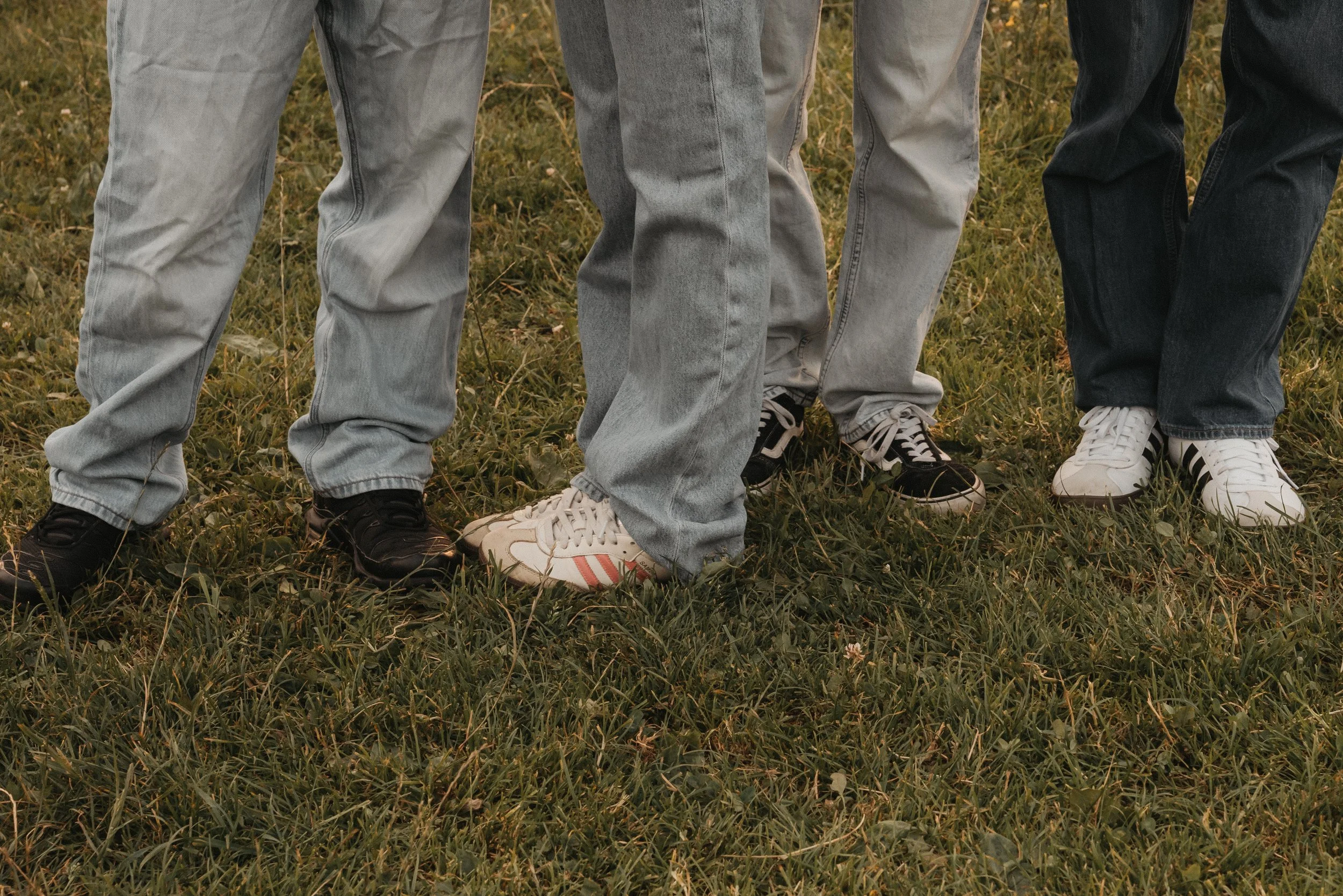 Menschen stehen nebeneinander auf einem grasbewachsenen Feld, nur ihre Beine und Schuhe sind sichtbar.