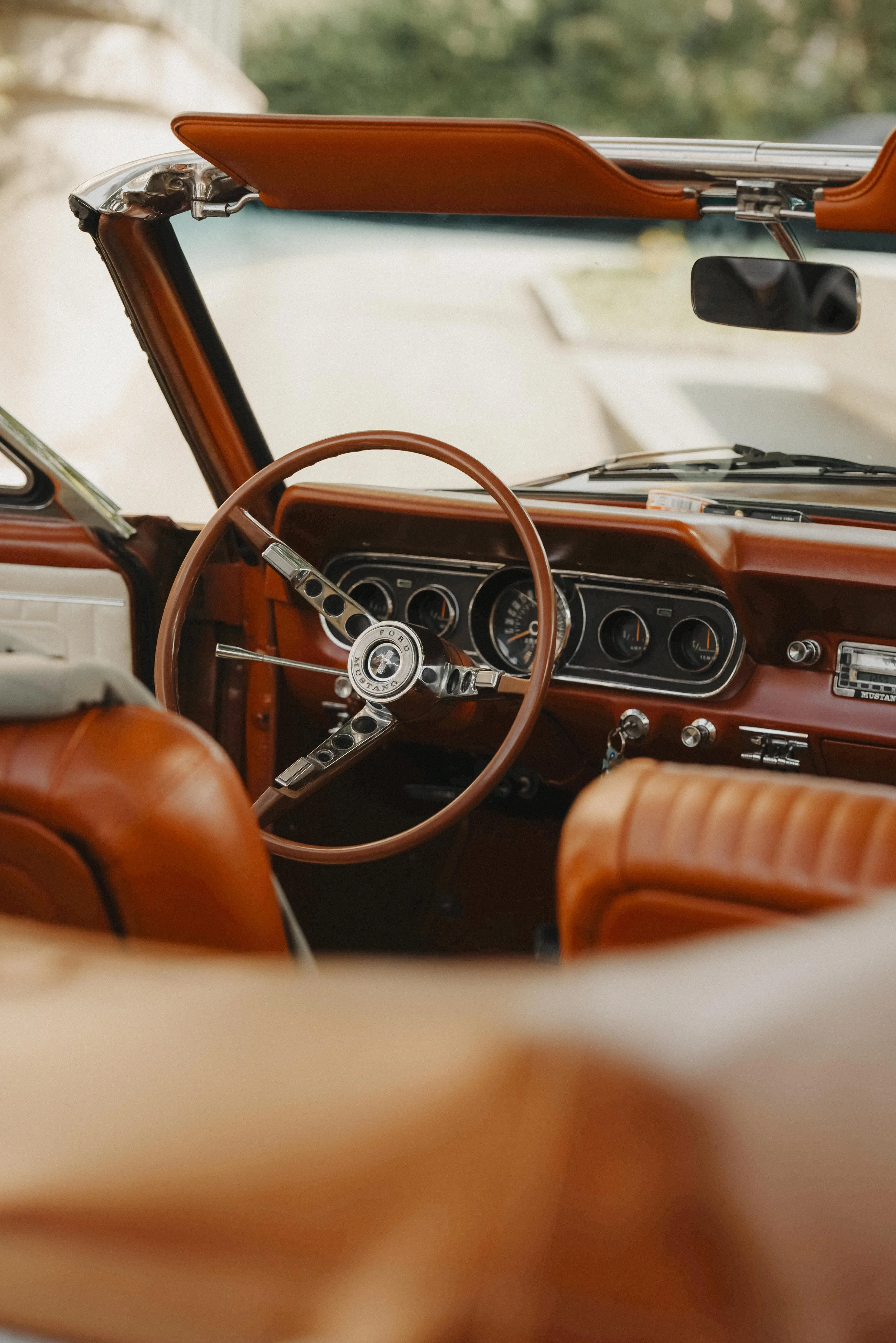 Ansicht des Innenraums eines klassischen Ford Mustang, mit braunem Lederlenkrad, Armaturenbrett mit runden Instrumenten und braunen Sitzen.