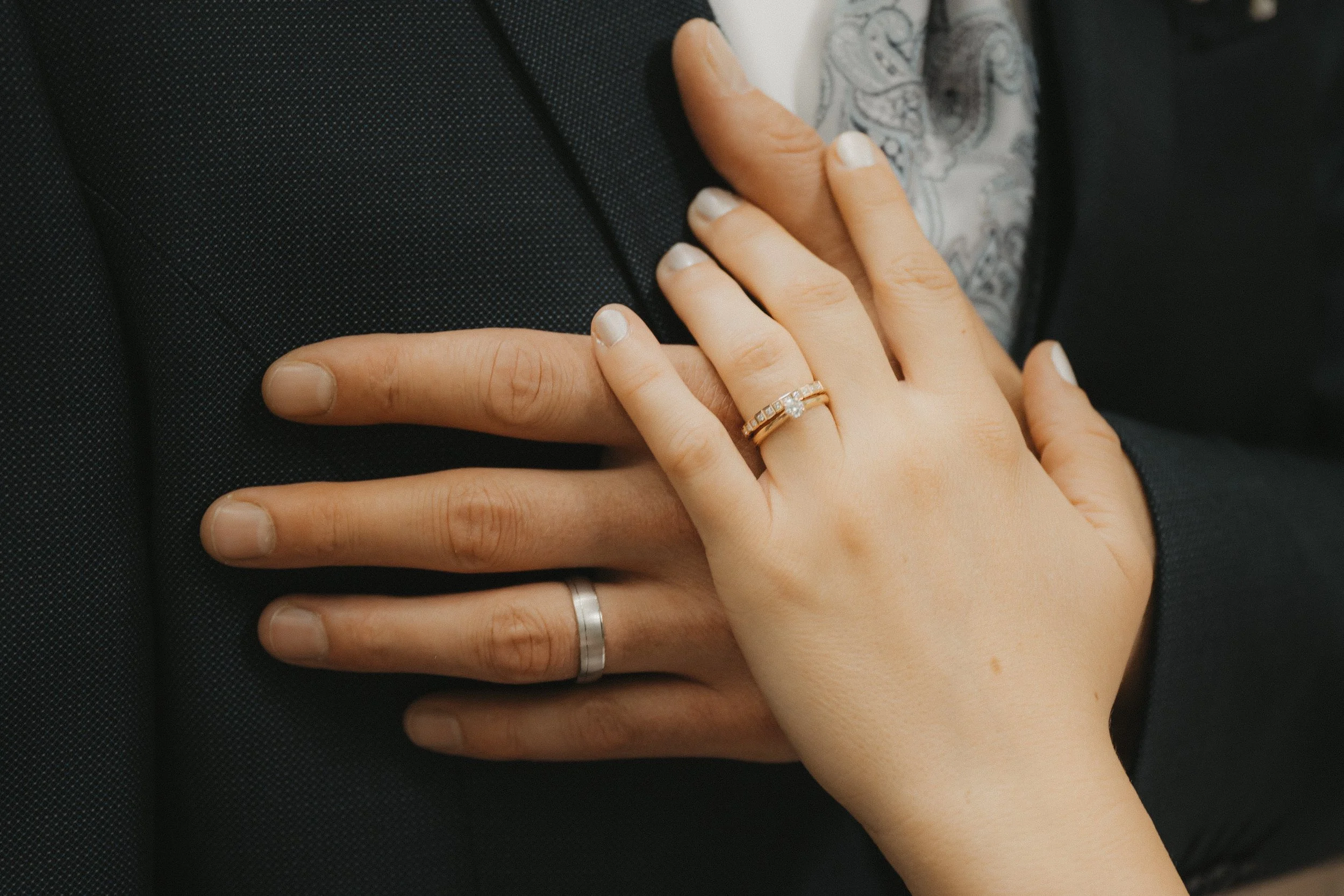 Nahaufnahme von einer Hand mit Ehering, die auf einer anderen Hand liegt, auf einem Anzug.