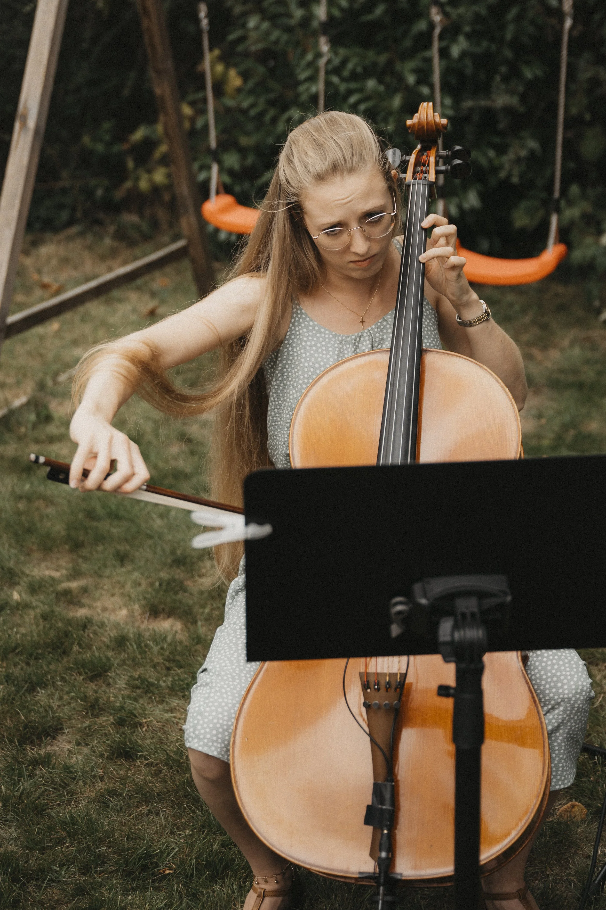 Junge Frau spielt Cello im Garten, im Hintergrund eine Schaukel.