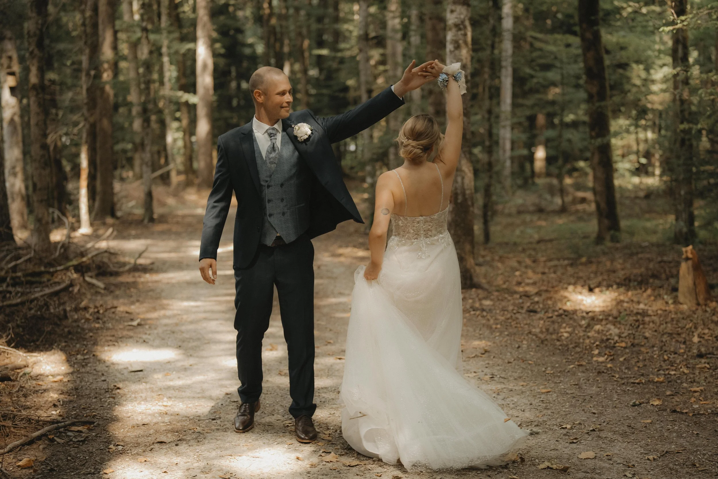 Ein Brautpaar tanzt im Wald, die Frau trägt ein weißes Hochzeitskleid und der Mann einen dunklen Anzug.