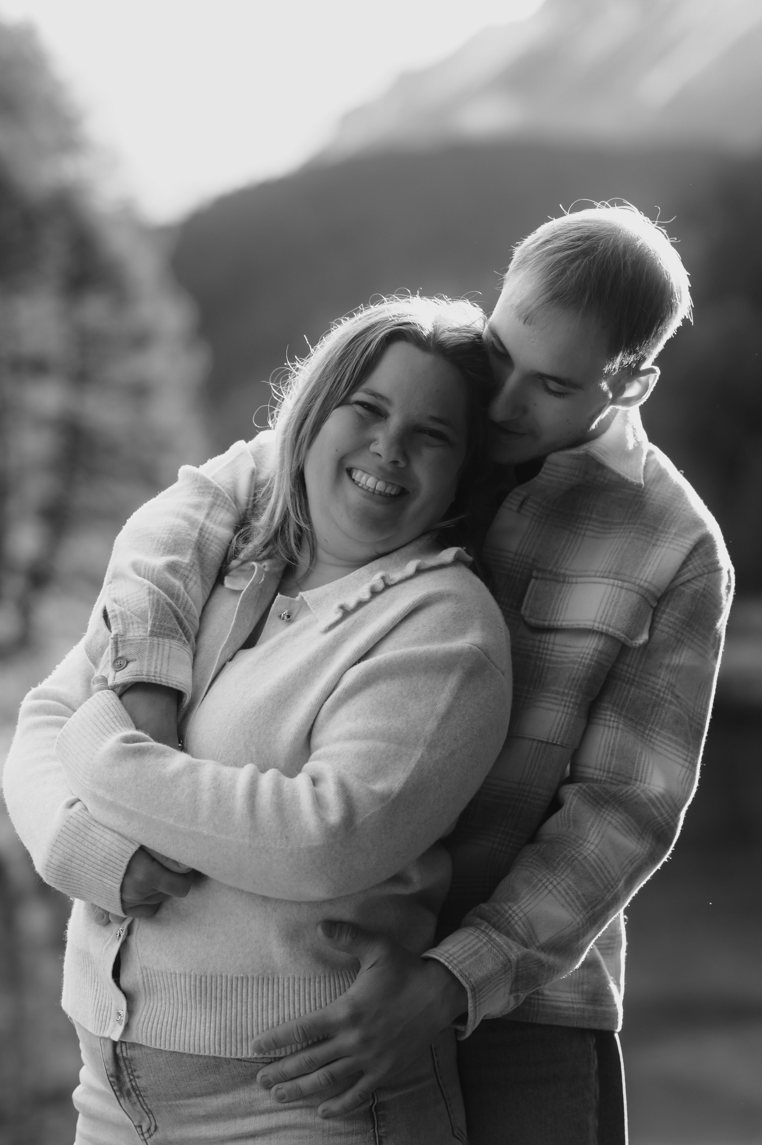 Ein lachendes Paar umarmt sich in einer natürlichen Kulisse, wahrscheinlich in den Bergen, im Schwarz-Weiß-Foto.