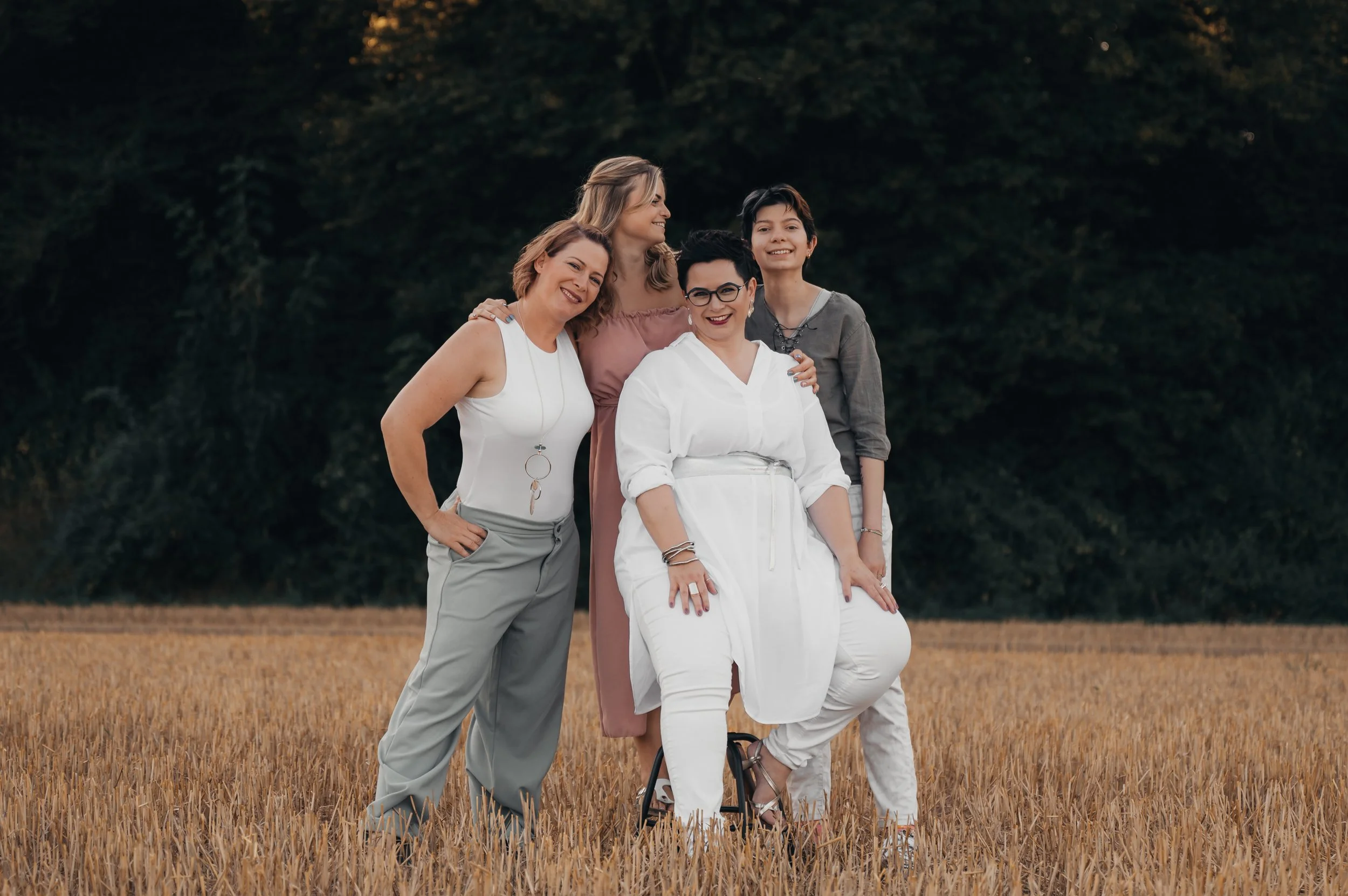 Fünf Frauen und ein Junge stehen lachend in einem goldenen Getreidefeld vor einem Baum. Es ist Nachmittag.