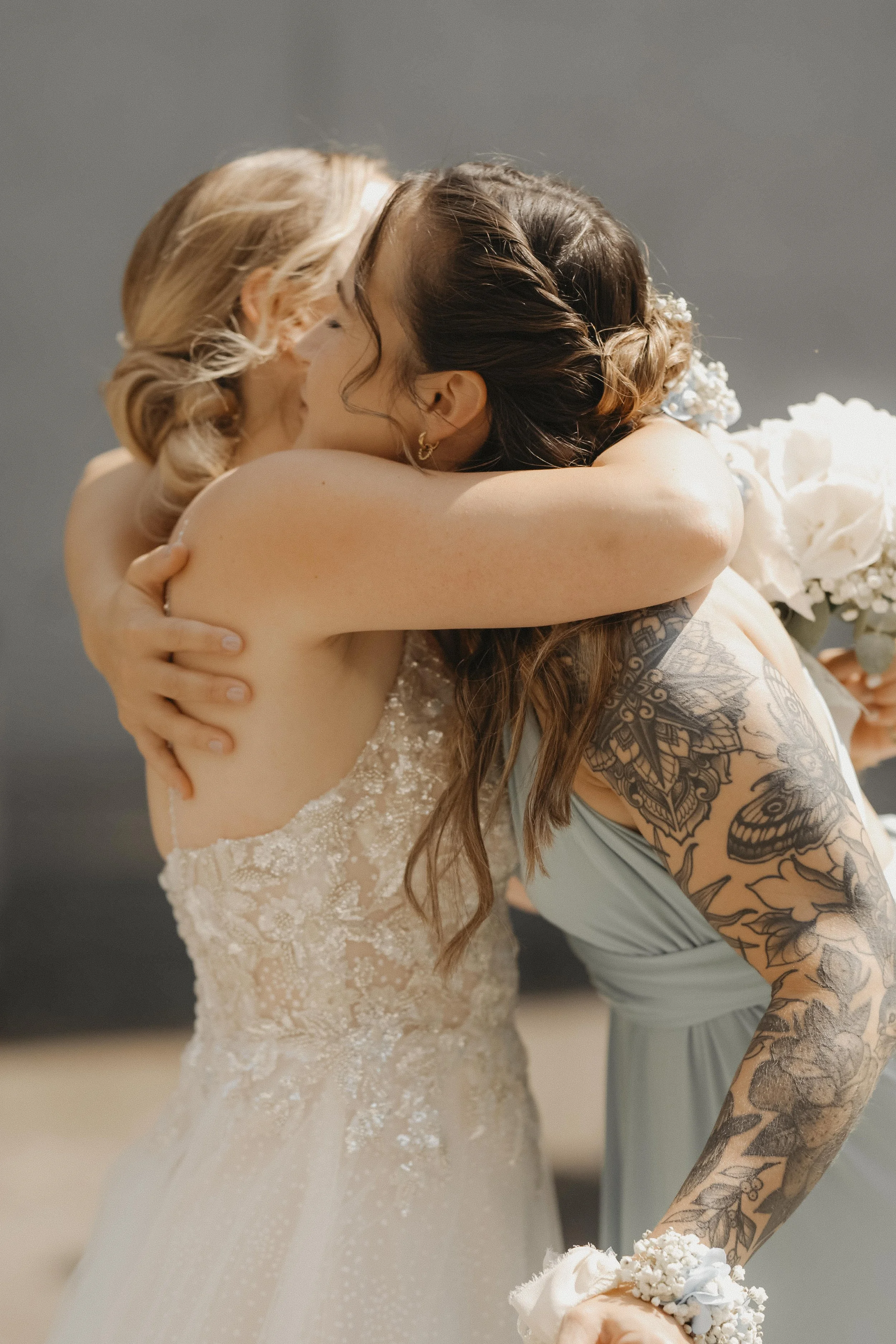 Zwei Frauen umarmen sich bei einer Hochzeit, eine trägt ein Brautkleid, die andere ein Brautstrauß, die Szene ist emotional und herzlich.