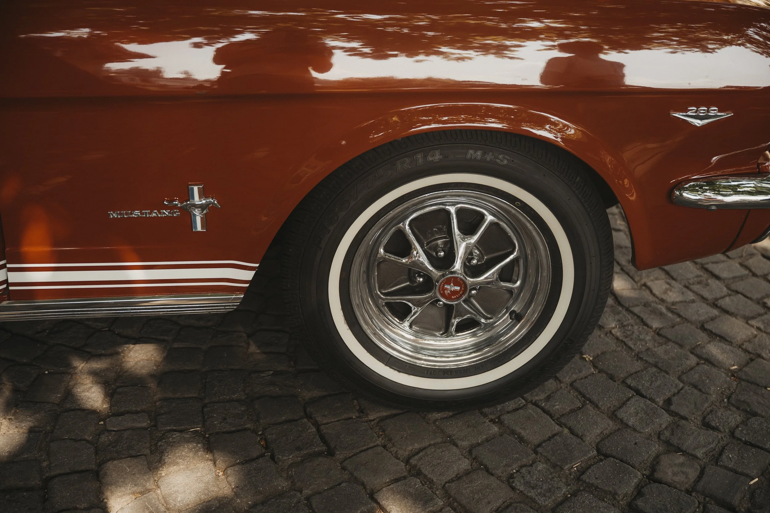 Nahaufnahme des vorderen rechten Rads eines roten Ford Mustang, mit weißen Reifen, auf einem gepflasterten Boden.