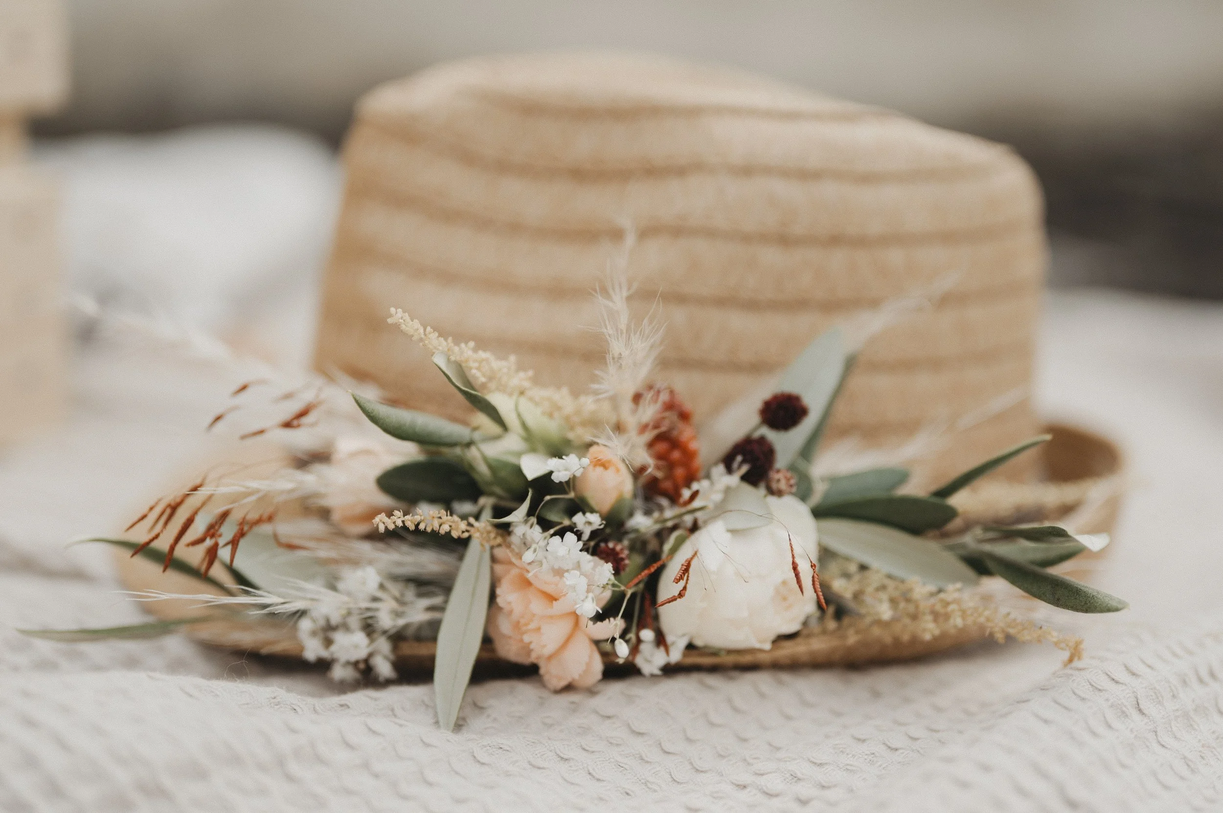 Ein Strohhut mit einer Blumen- und Pflanzenfrisur auf einem weißen Stoff.