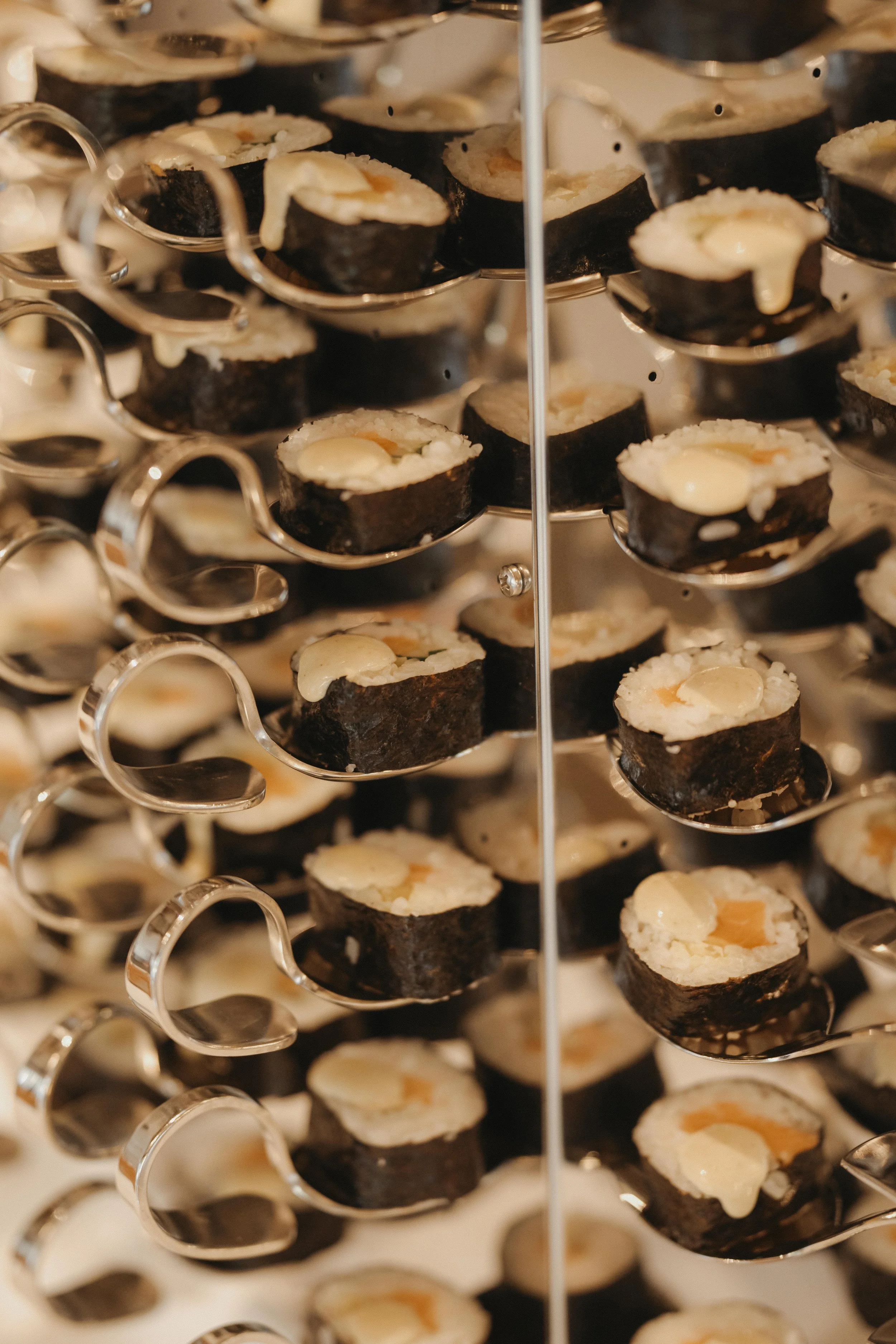 Nahaufnahme von Sushi-Röllchen mit schwarzem Seetang, Reis und Ei auf kleinen Metalllöffeln, gestapelt auf einem mehrstöckigen Serviertablett.