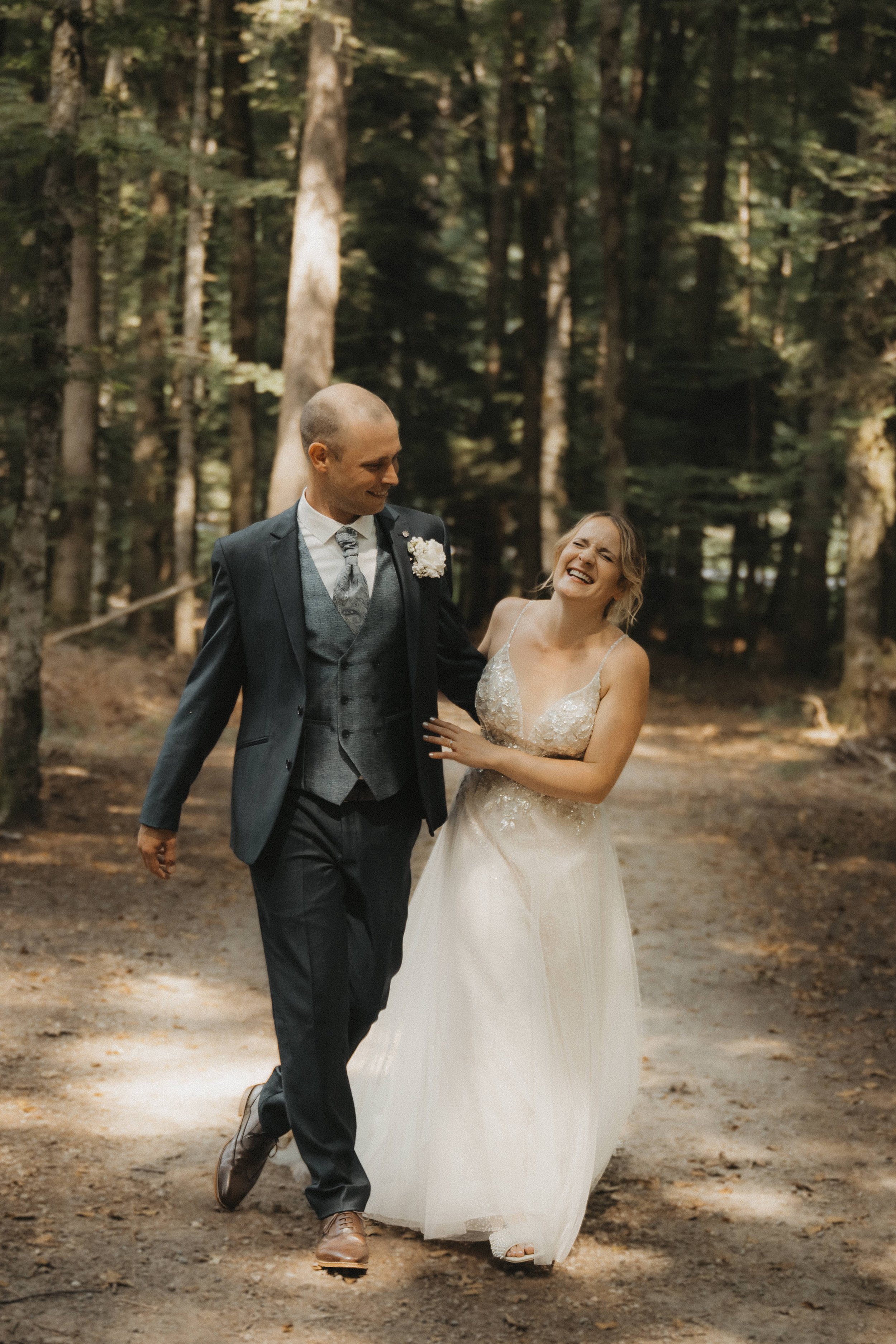 Ein glückliches Hochzeitspaar, das zusammen durch einen Wald spaziert, lachend und sich liebevoll zugewandt.