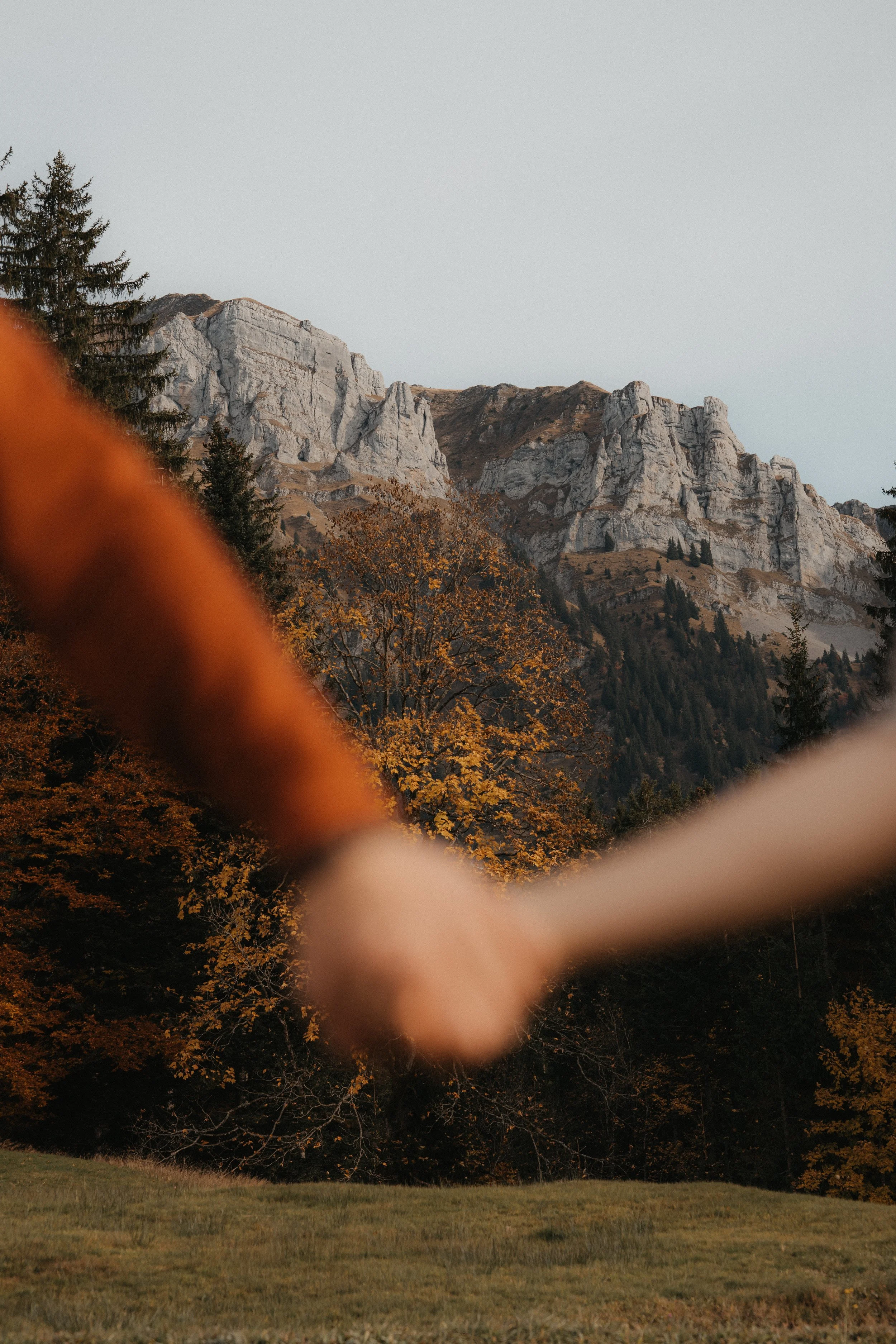 Zwei Menschen halten sich an den Händen, im Hintergrund sind Berge und herbstliche Bäume sichtbar.