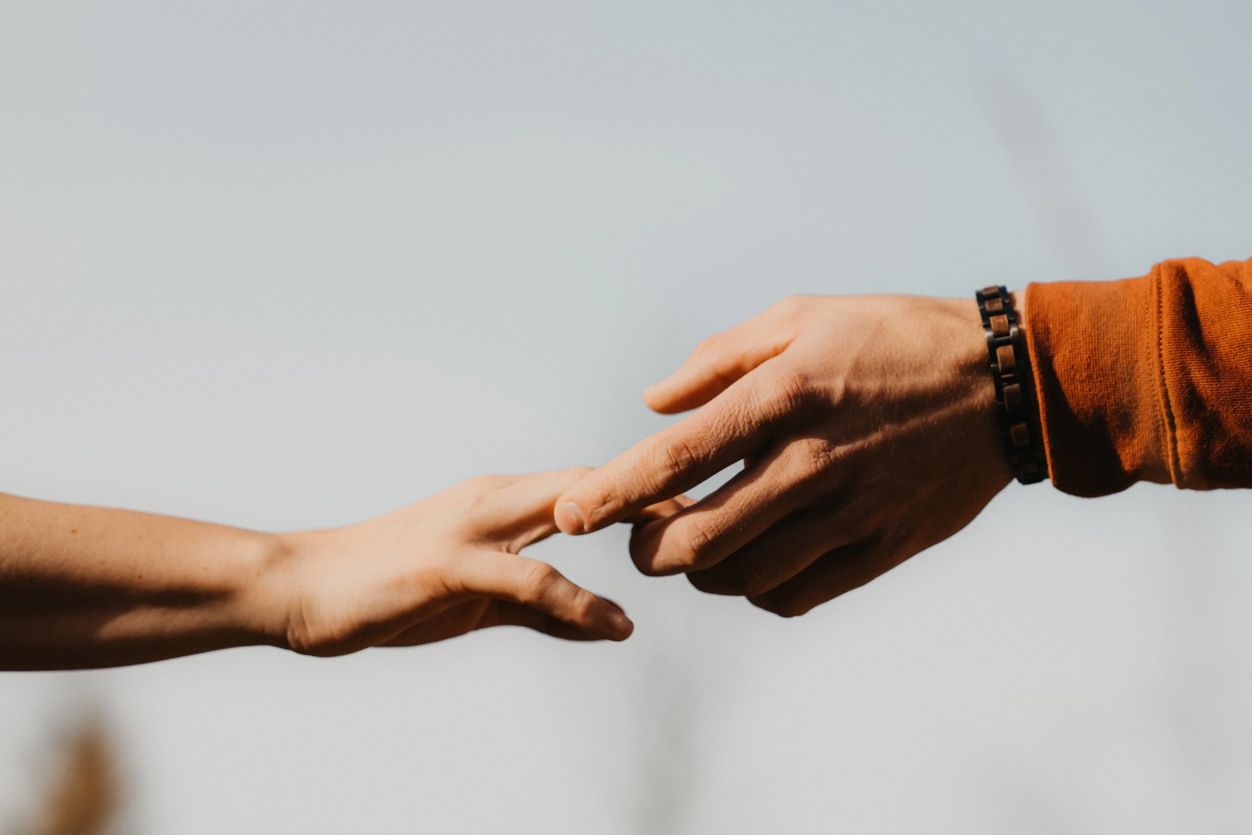 Nahaufnahme von zwei Händen, die sich fast berühren, mit einem hellen Himmel im Hintergrund.