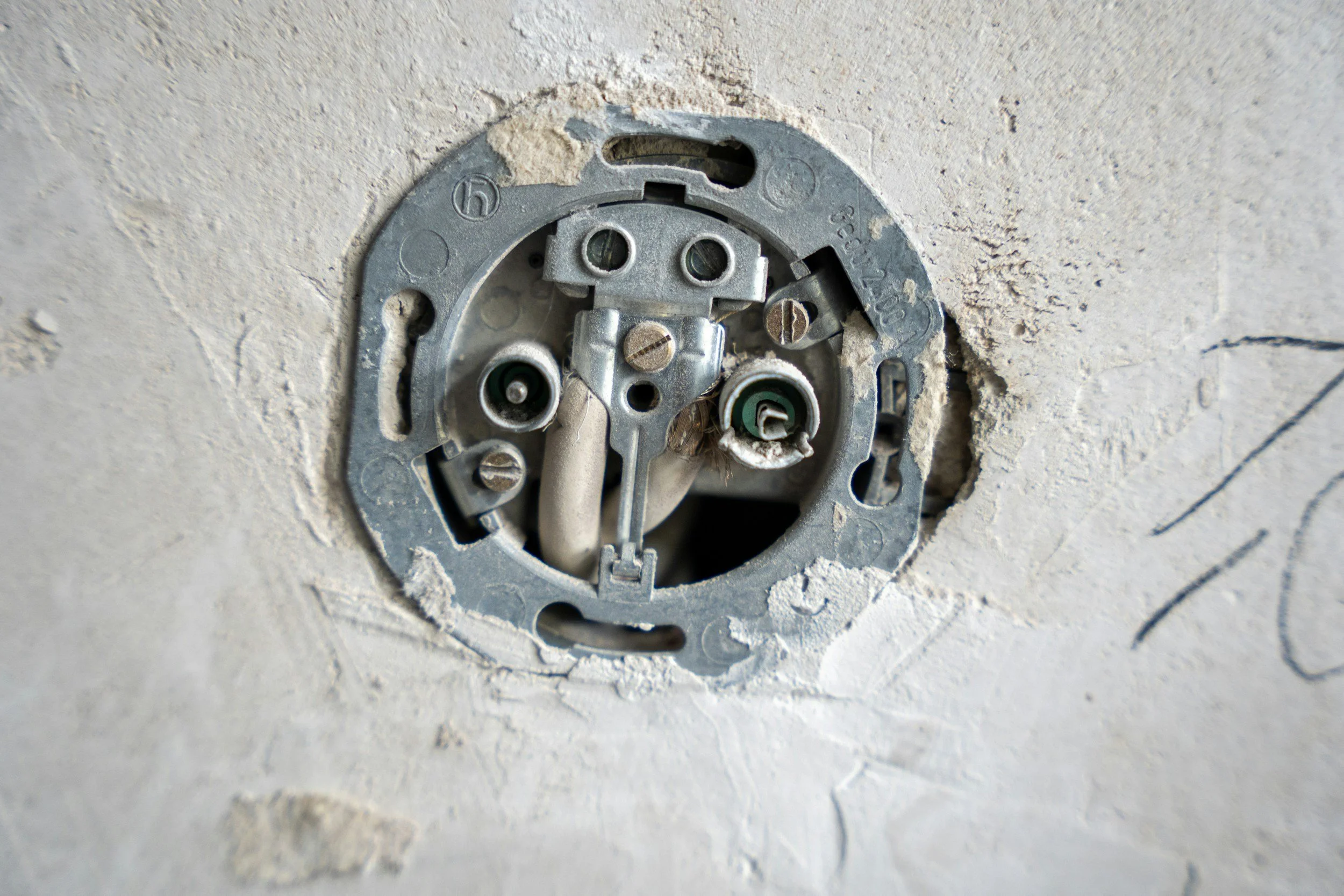 Close-up of a recessed electrical outlet box in a wall with exposed wiring and mounting hardware.