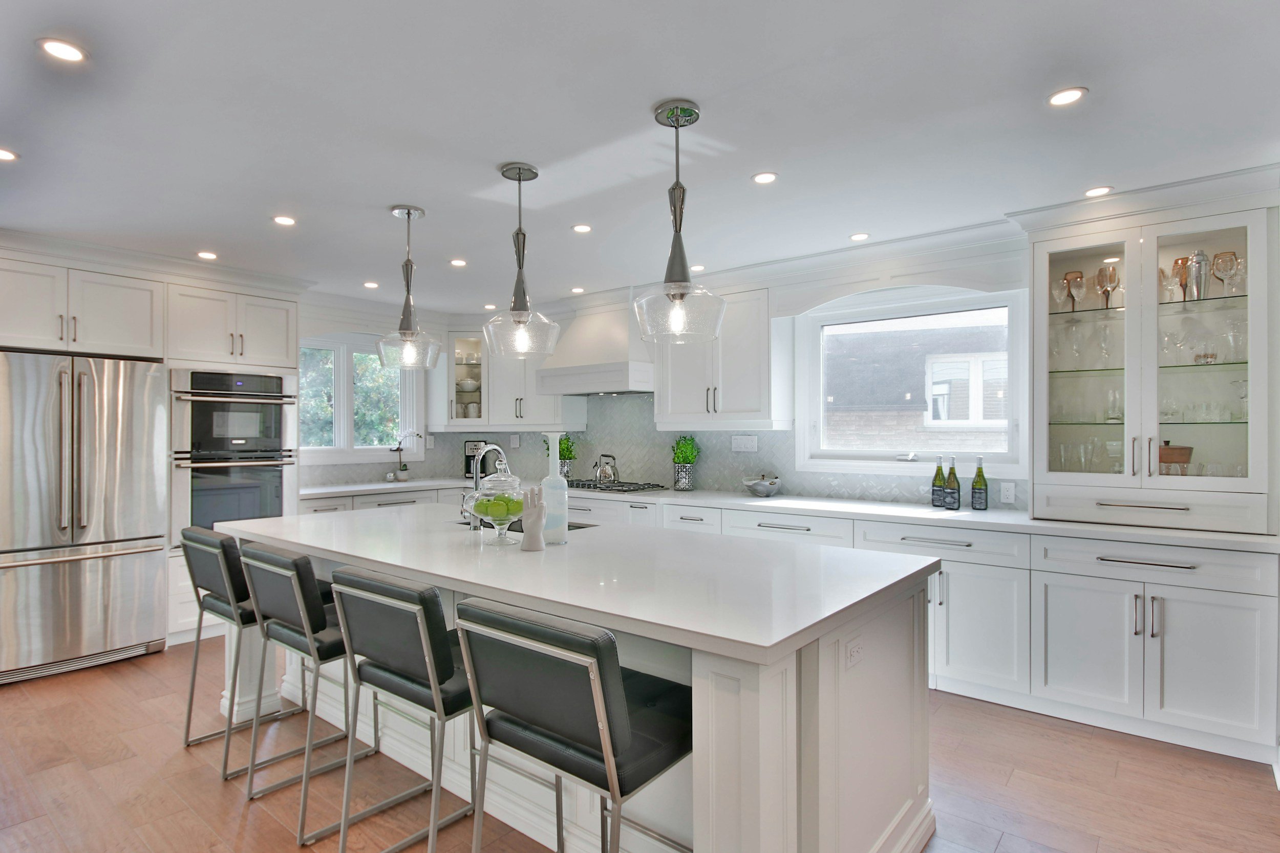 Bright white kitchen with island, black chairs, stainless steel refrigerator, cabinetry, and large window.