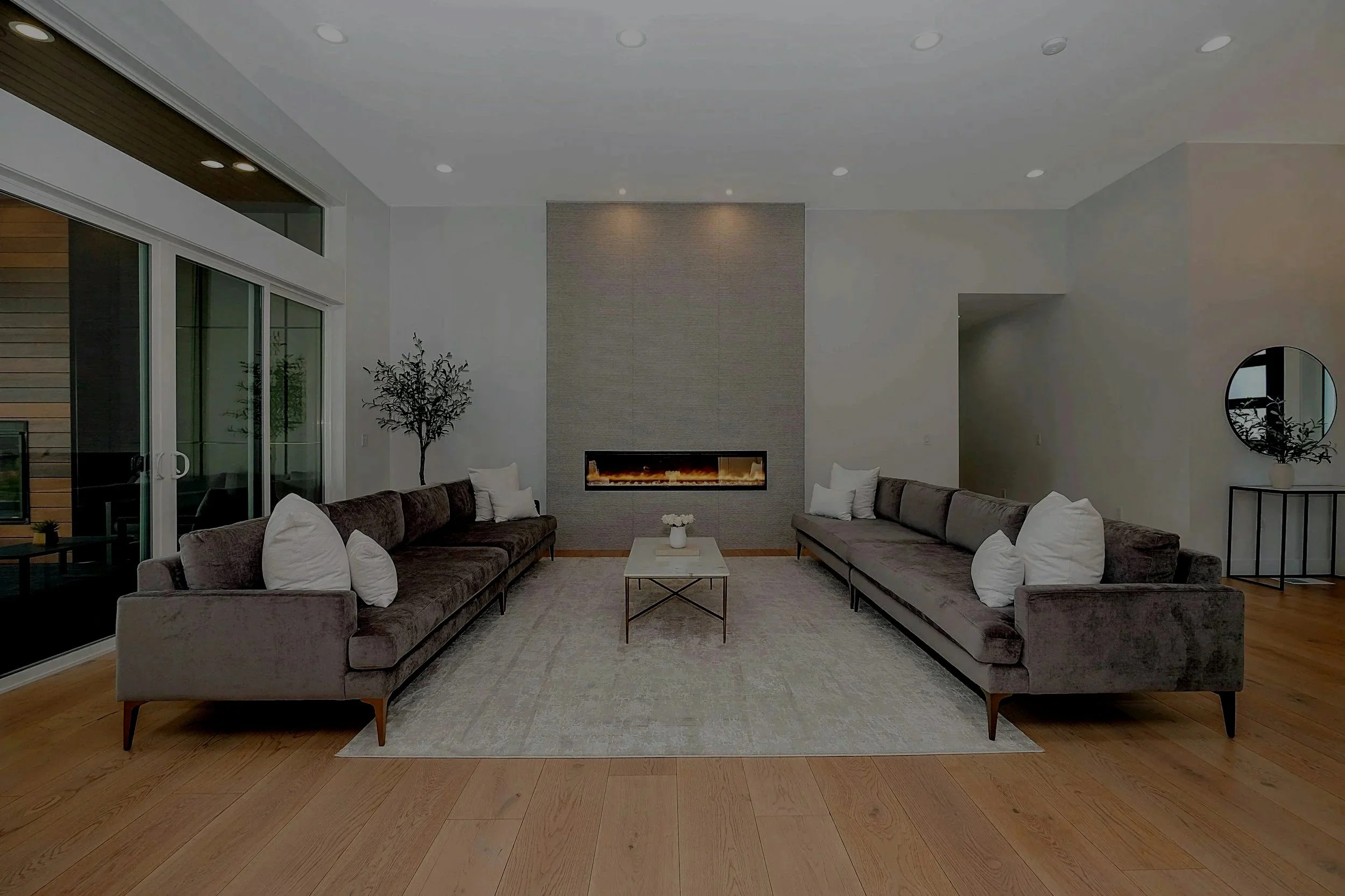 Living room with two long sofas facing each other, a central coffee table, a fireplace on a textured wall, and sliding glass doors leading outside.