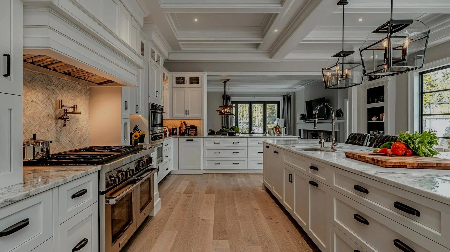 Modern kitchen with white cabinetry, marble countertops, and hardwood floors. Features a large island, stainless steel stove, and multiple pendant lights. Bright space with large windows and a view of the outdoors.