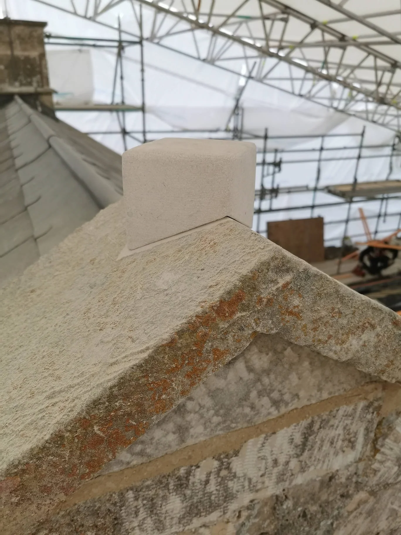 Close-up of a brick wall with a white mortar cap at a construction site, with scaffolding and a roof structure in the background.