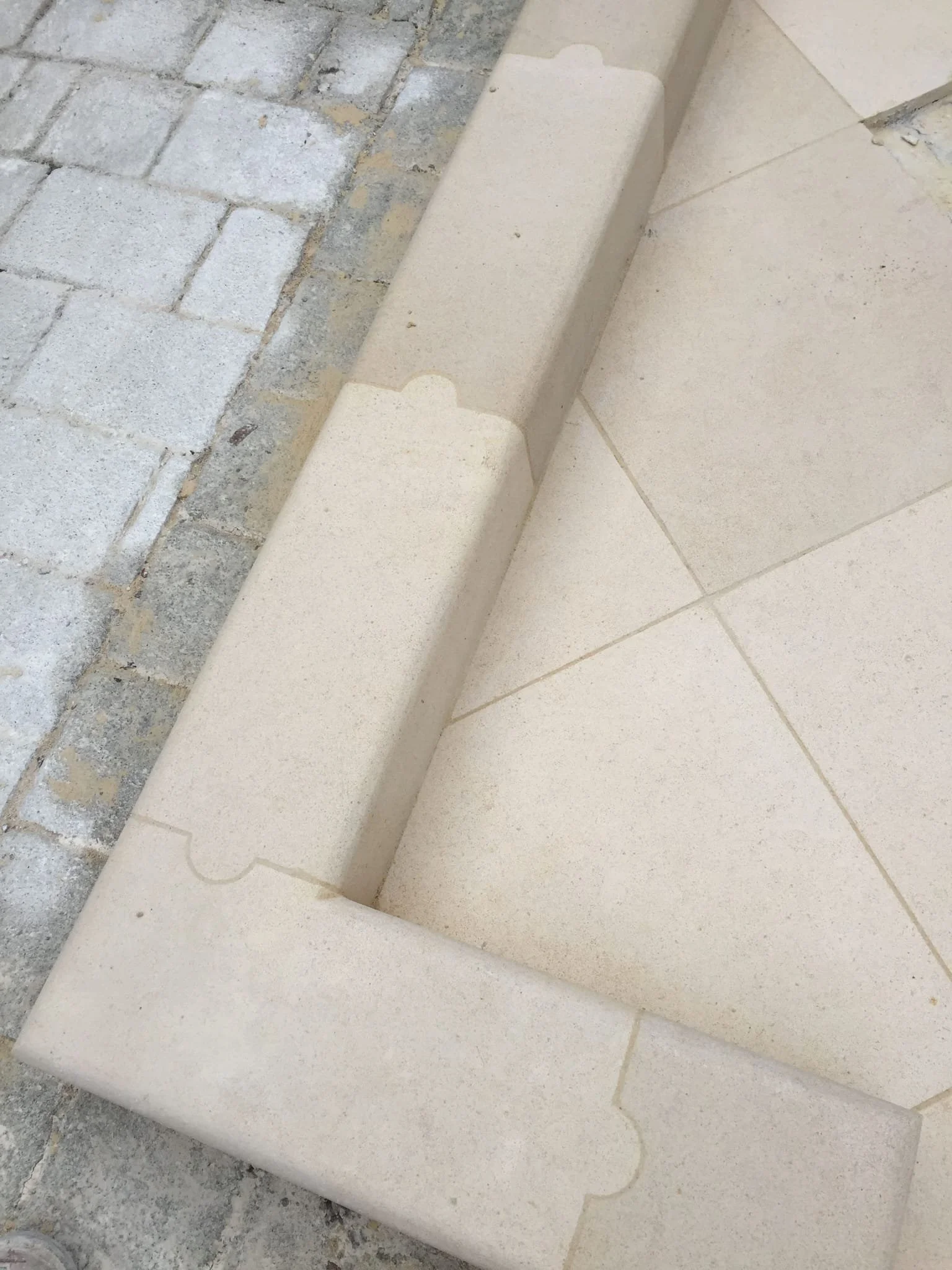 Close-up of a beige stone step with detailed grooves, next to a brick walkway.