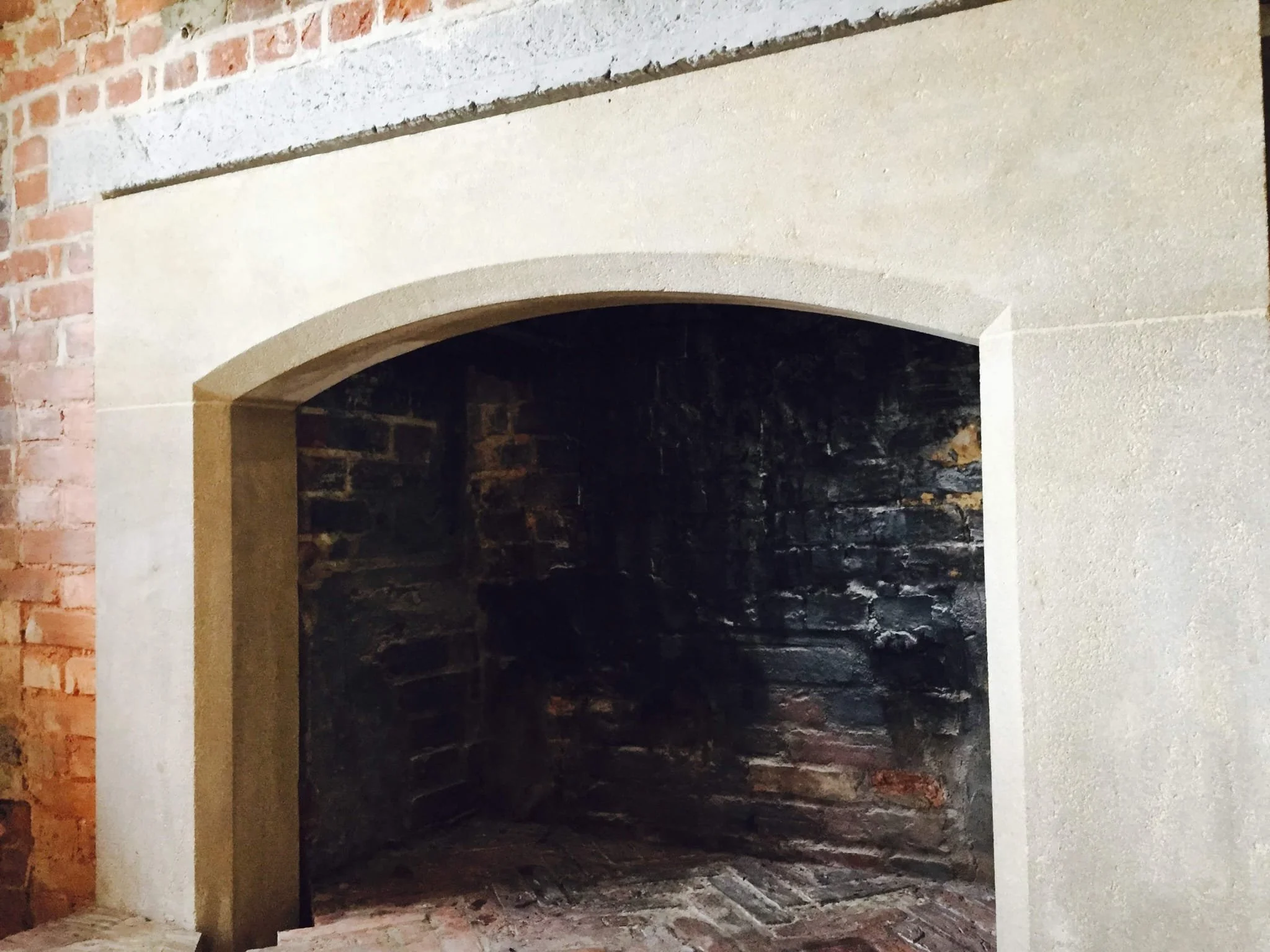 Close-up of a brick fireplace with an arched cream-colored stone surround and a dark interior showing brick and stone.
