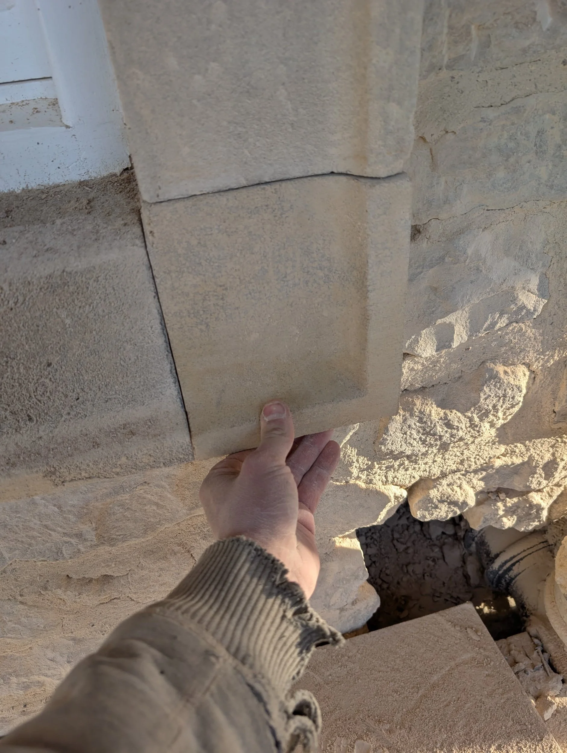 Person holding a sandstone brick in front of a stone wall construction site.