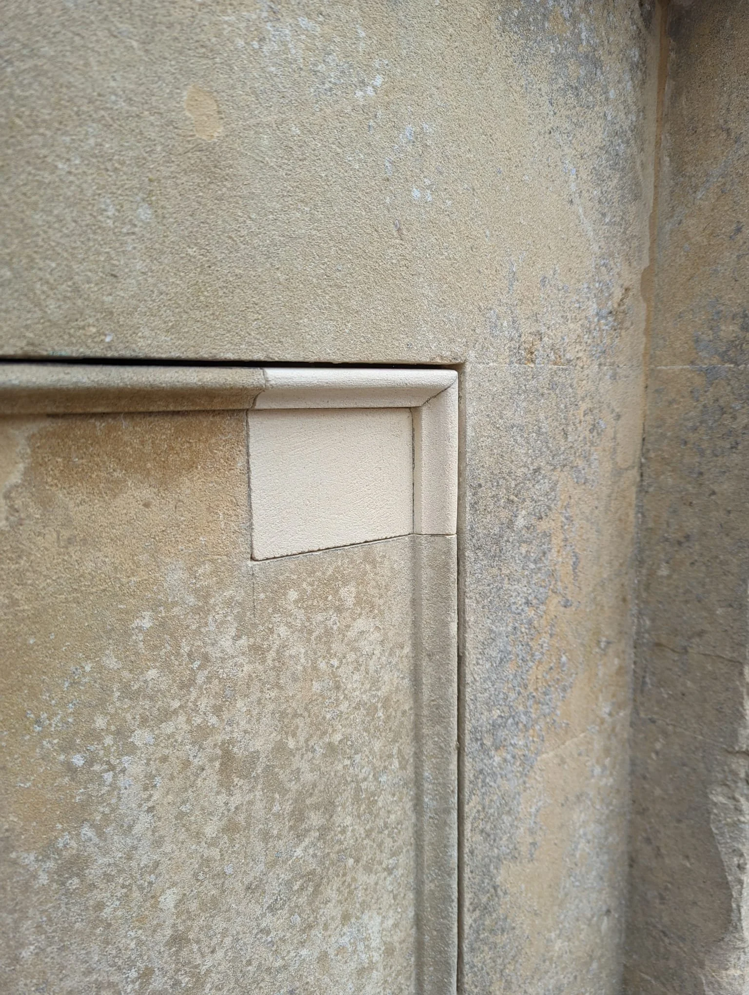 Close-up of beige tiled wall with a small concealed door or panel.