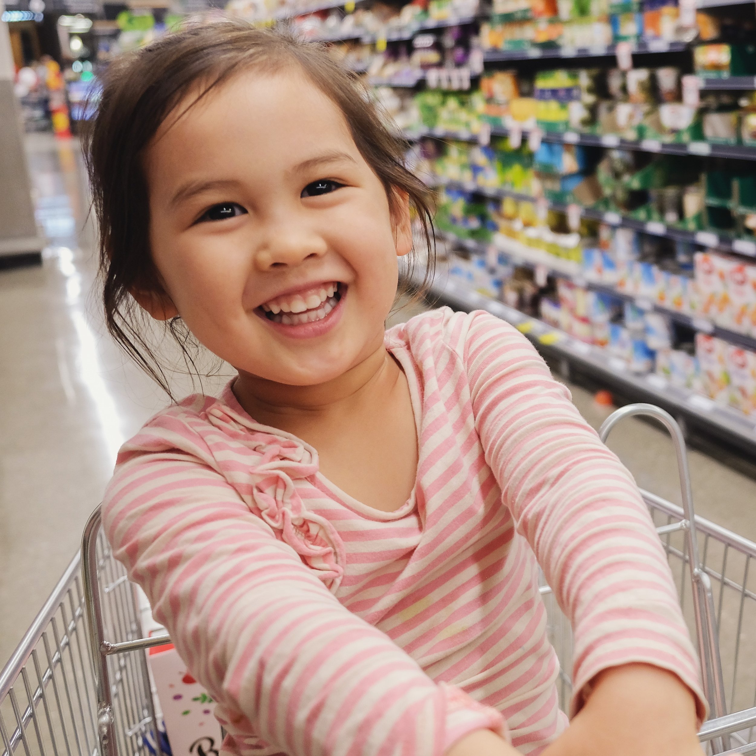 Young child smiles while sitting in a grocery cart