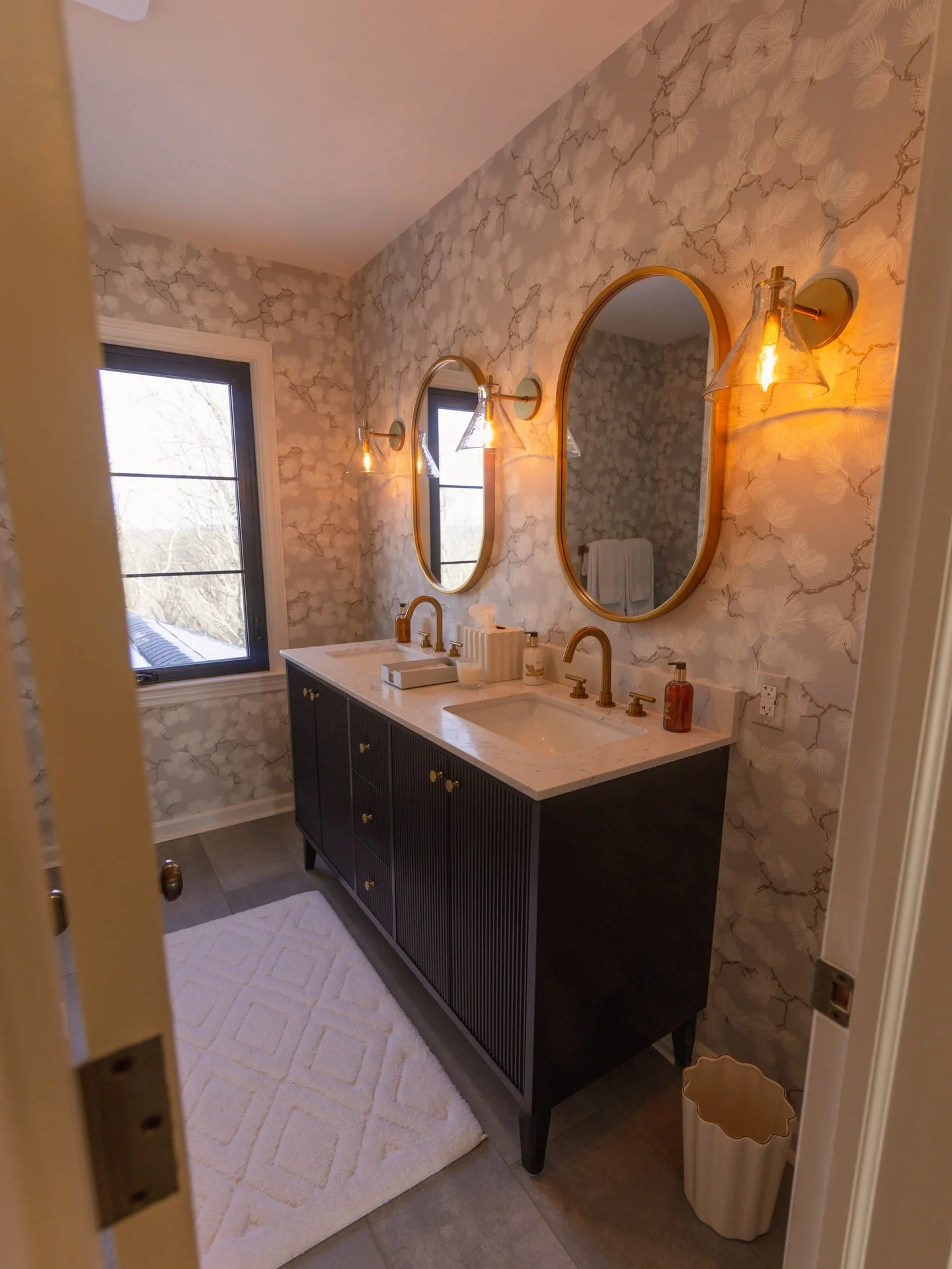 Every home project is defined by the little details that bring everything together. 

This homeowner chose to customize their space with patterned wallpaper, sconce lighting, and a monogrammed shower curtain. Complete with brush gold hardware and a b