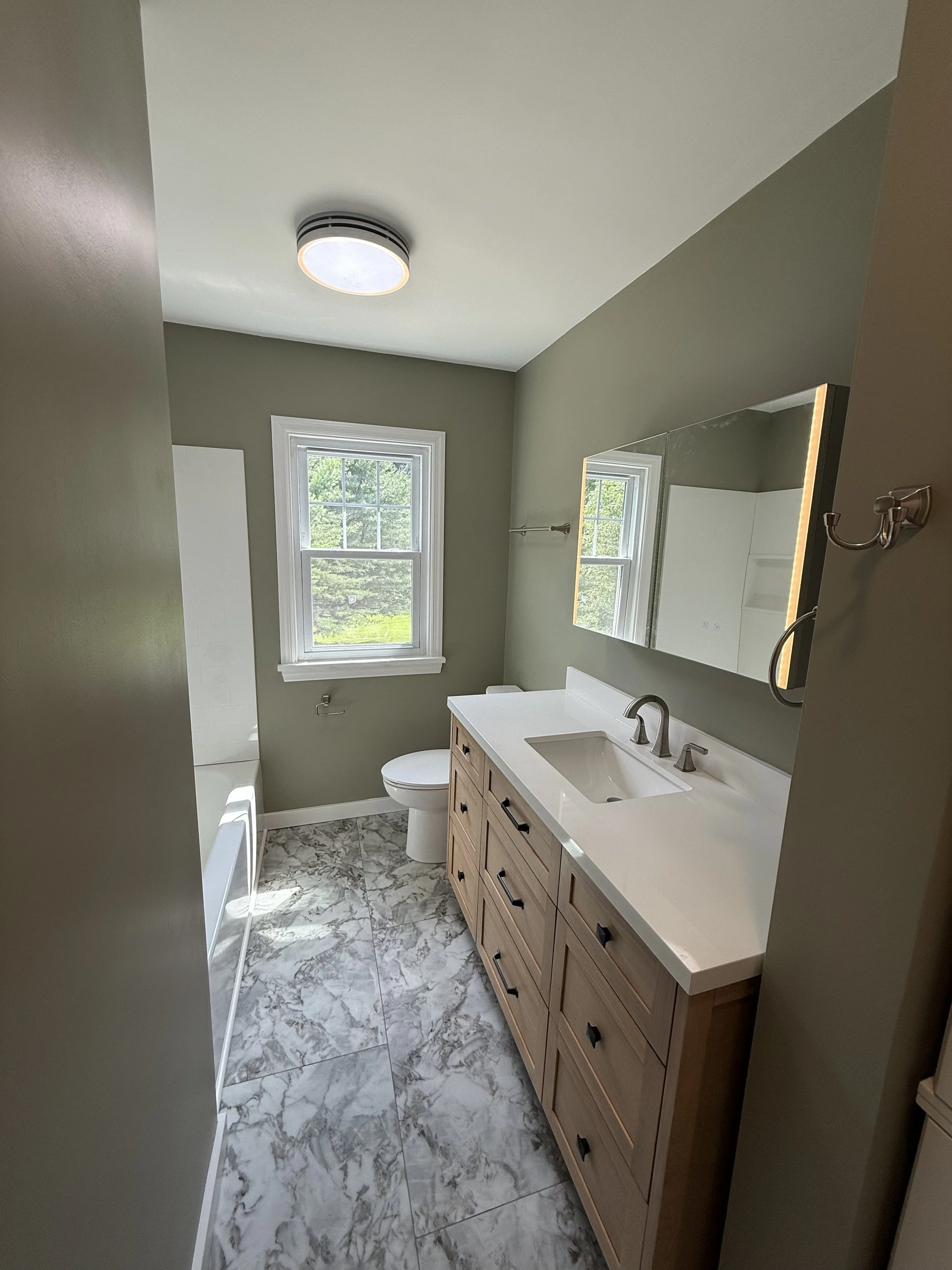 Bathroom with two windows, a white vanity with a sink, a large mirror, a toilet, a tub, and marble flooring.