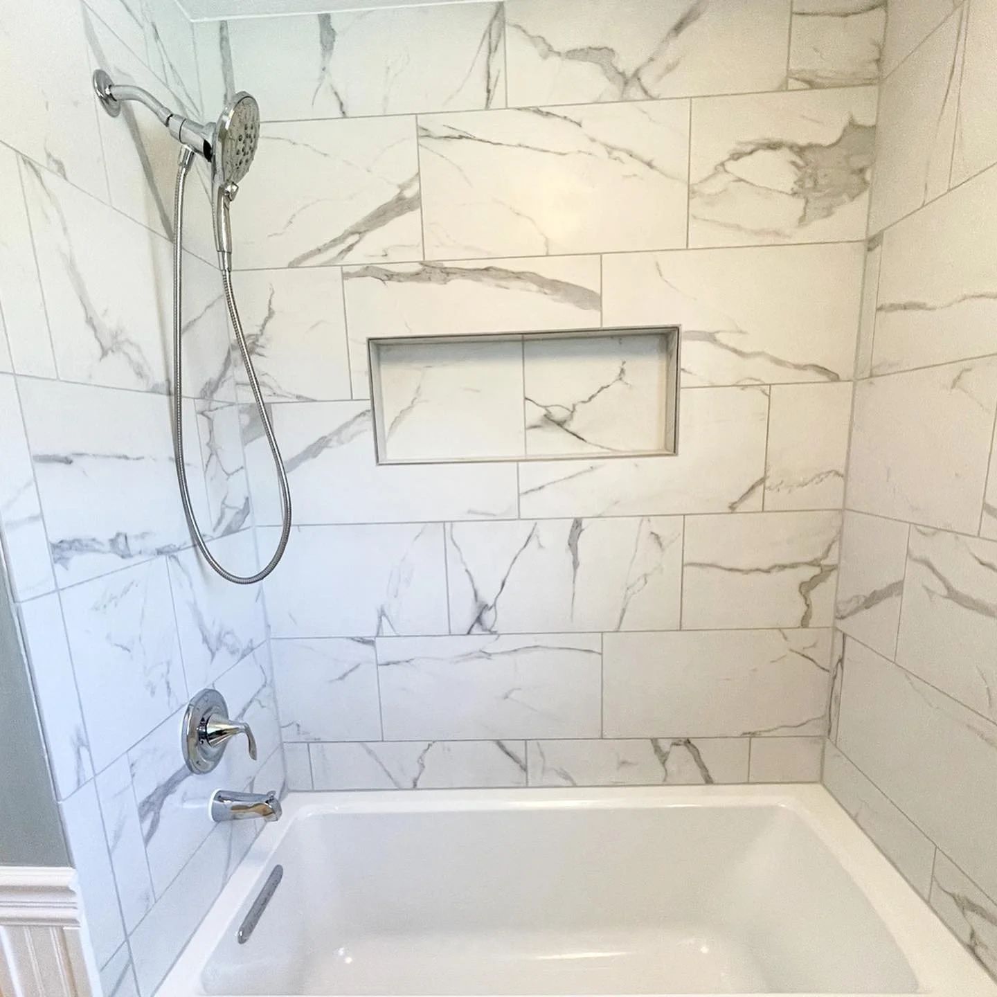 Bathroom shower with marble tiles, a built-in niche, a handheld showerhead, and a bathtub.