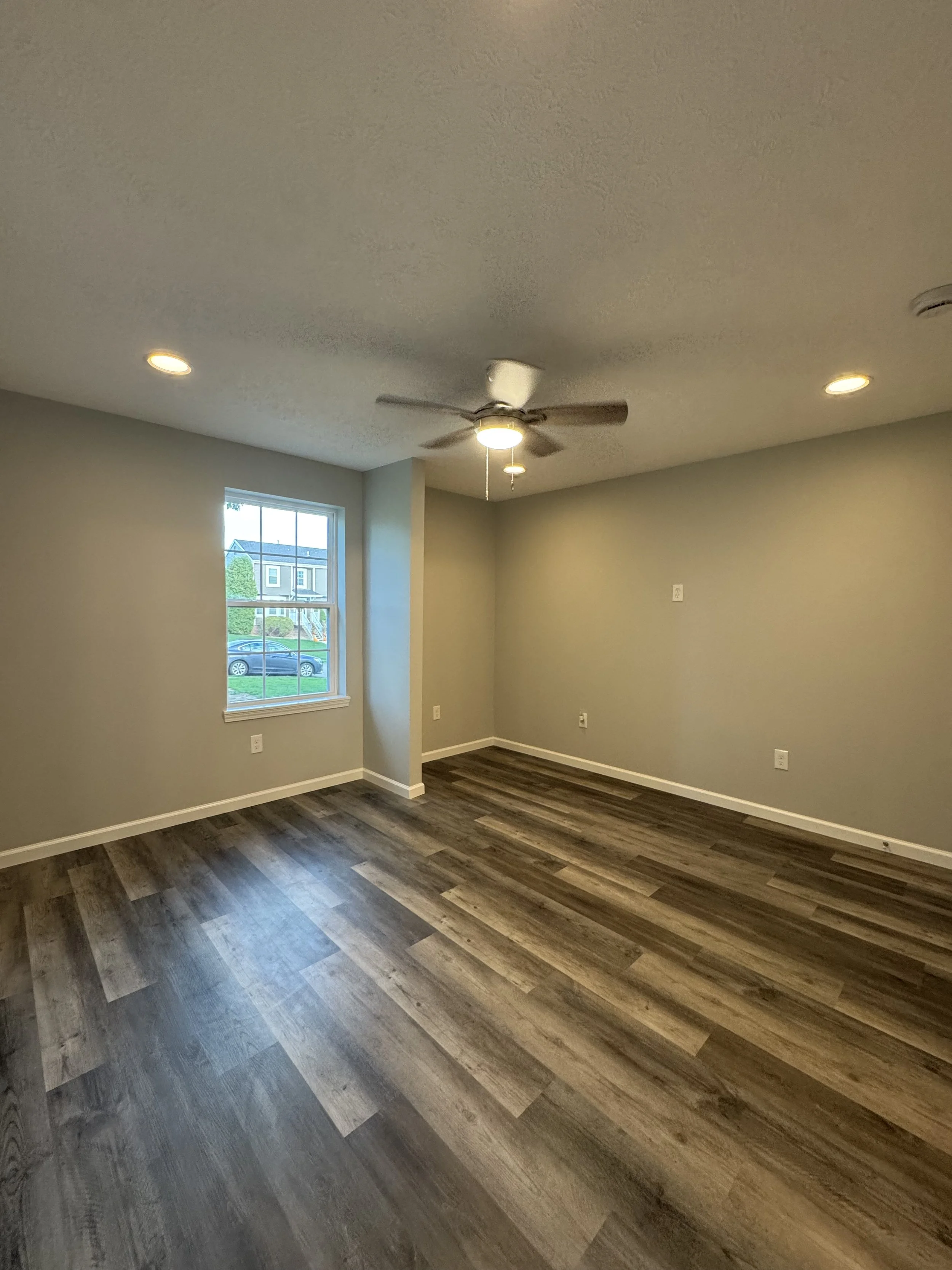 Empty room with wood flooring, a window, ceiling fan, and recessed lighting.