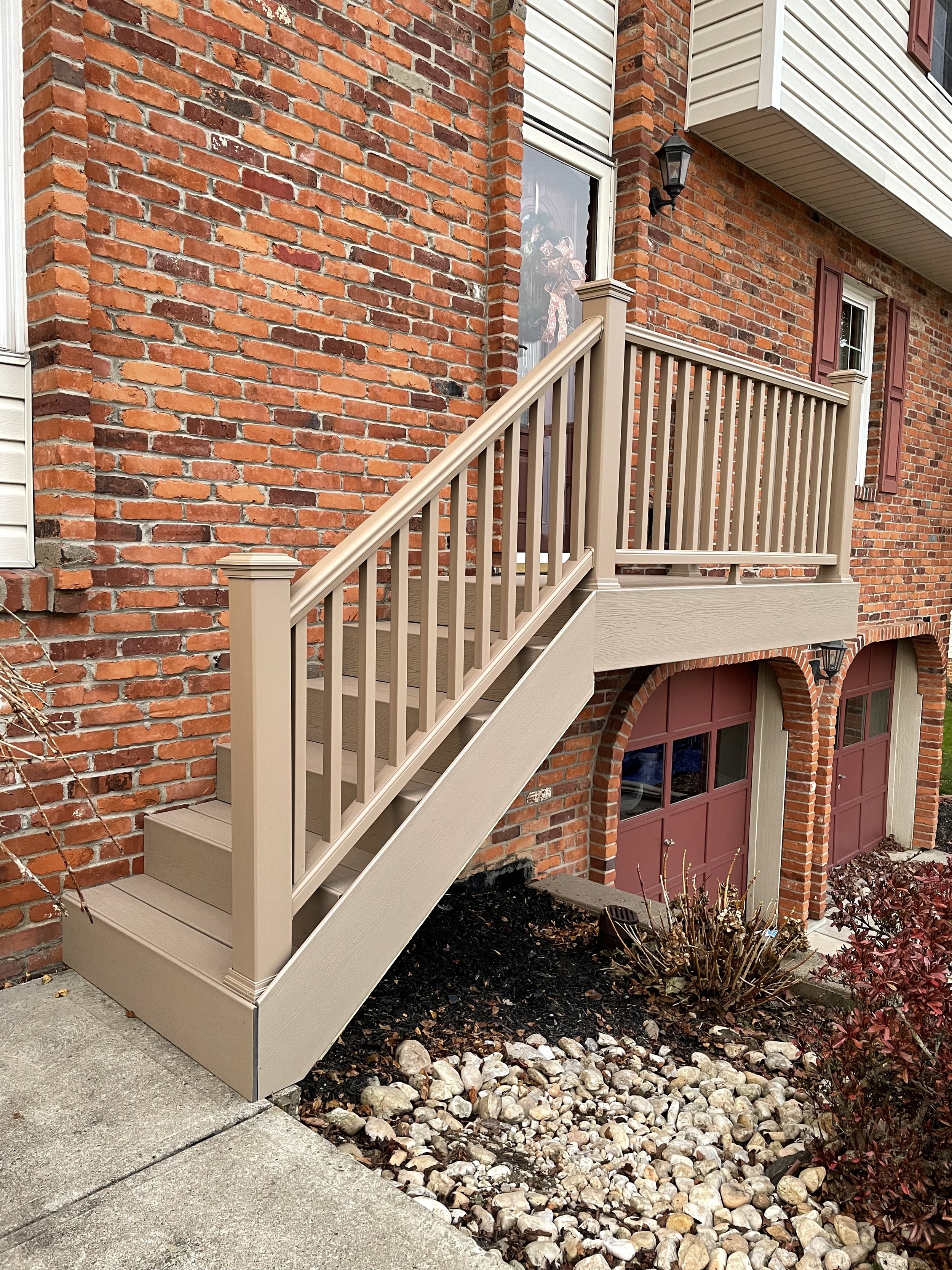 A beige wooden staircase leading to a door on the upper level of a red brick house with arched garage doors below.