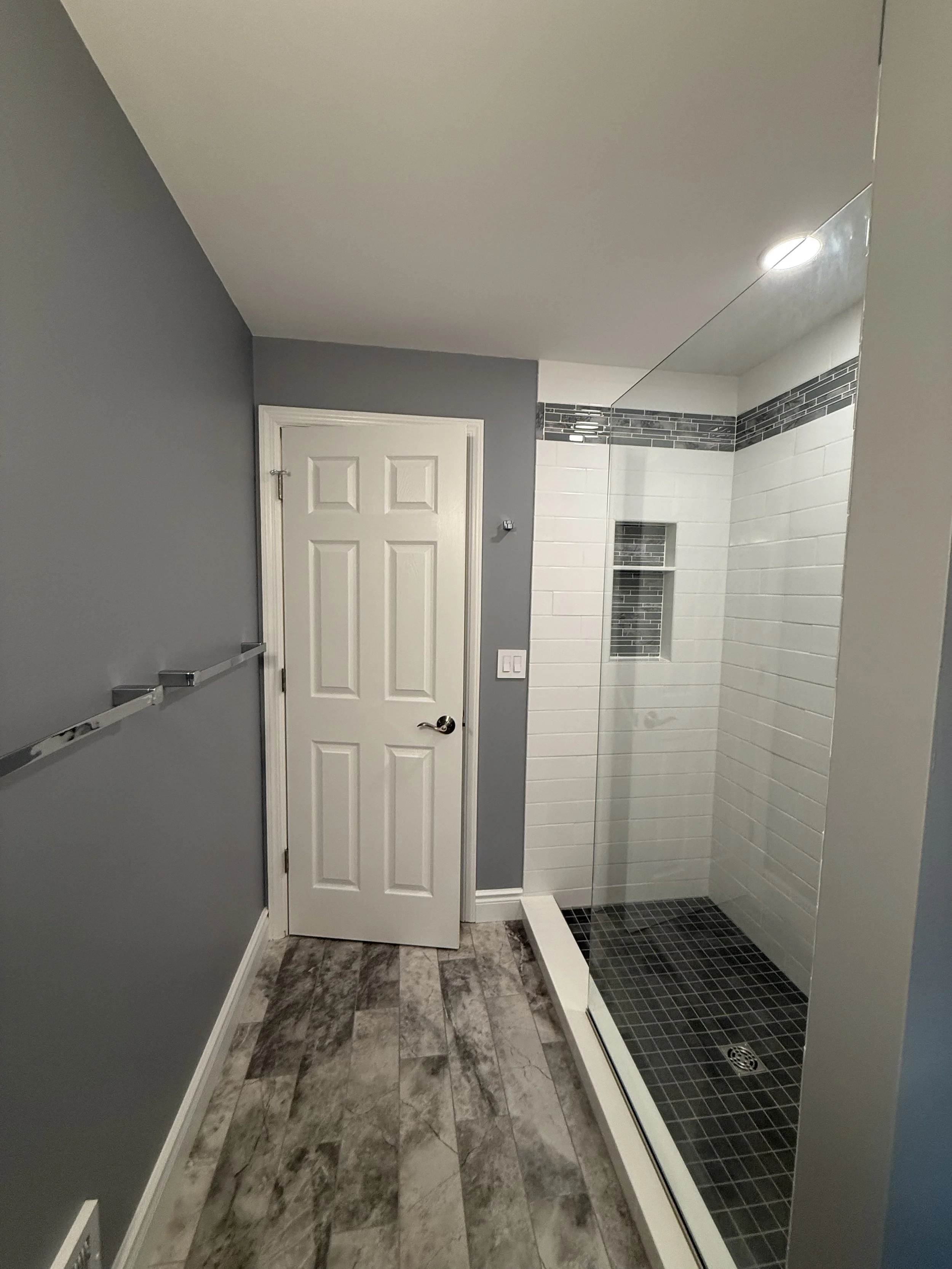 Bathroom with gray walls, a white door, and a glass-enclosed shower stall with black and white tiles.