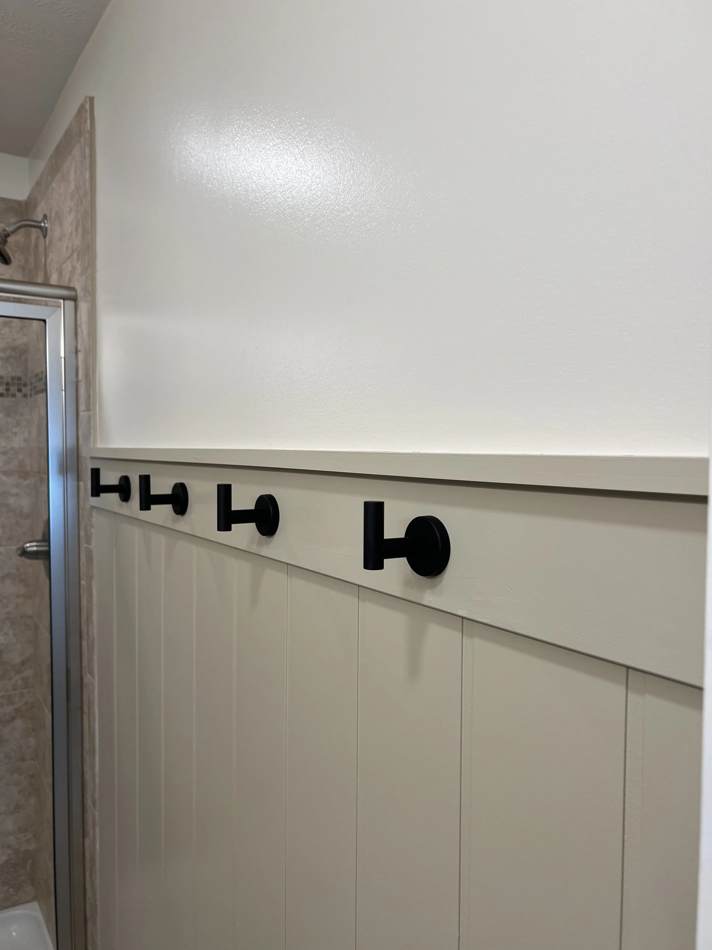 Bathroom wall with black hooks for hanging towels or clothes.