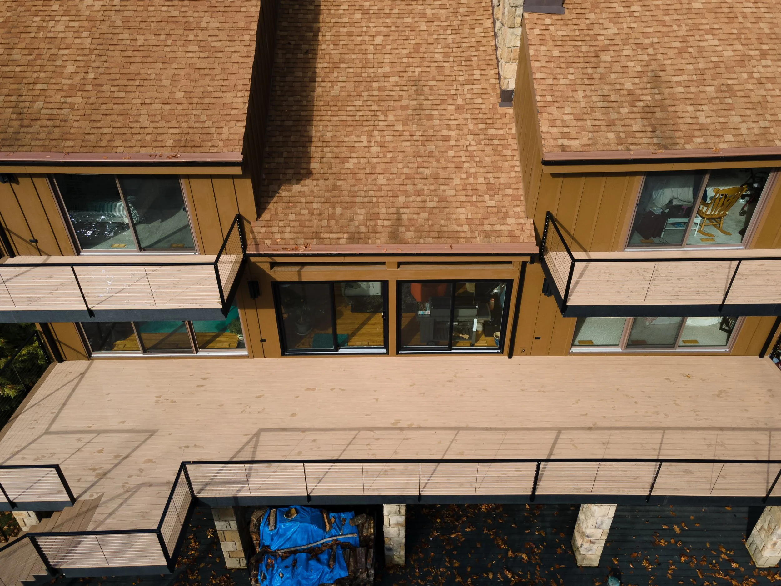 Aerial view of a multi-story building with a wood deck, sliding glass doors, and balconies with metal railings, with a sloped roof and autumn leaves on the ground.
