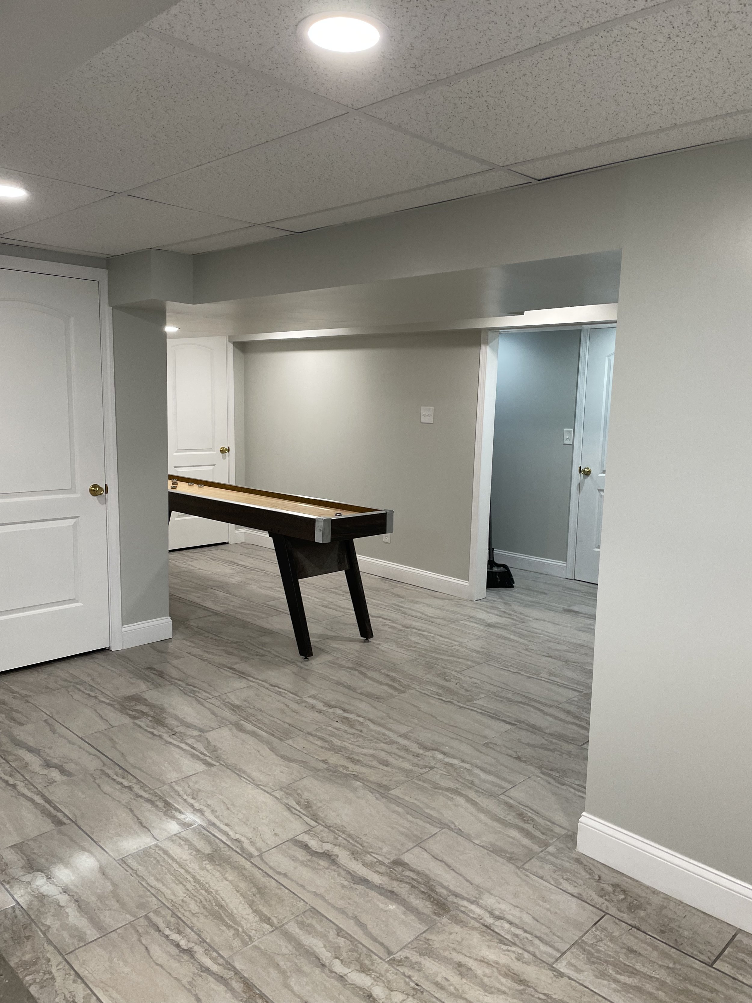 Empty basement room with beige tiles, white doors, and a partially assembled foosball table.