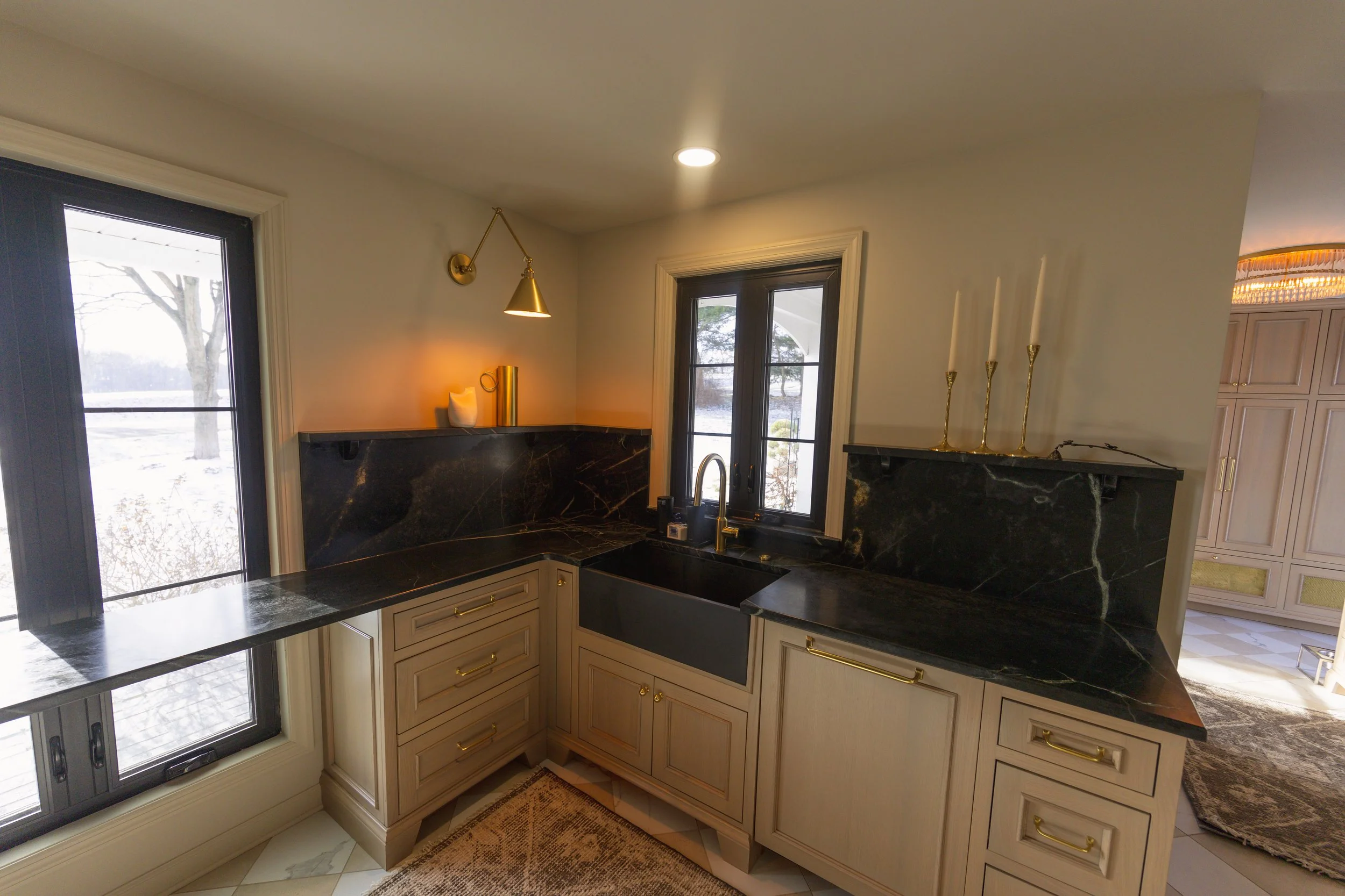 Kitchen with black marble countertops, cream cabinets with gold handles, black sink, window above sink, and a sliding door to the outside.