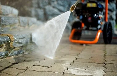 A hose spraying water onto a paved stone surface with a vehicle in the background.