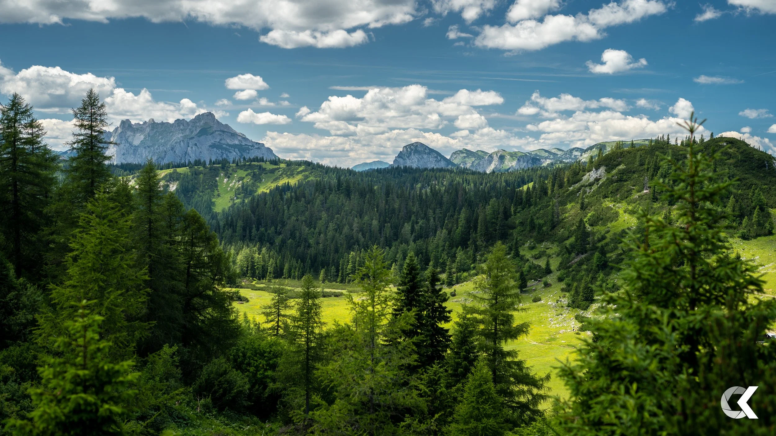 Lush green forested mountains under a clear blue sky with scattered clouds.