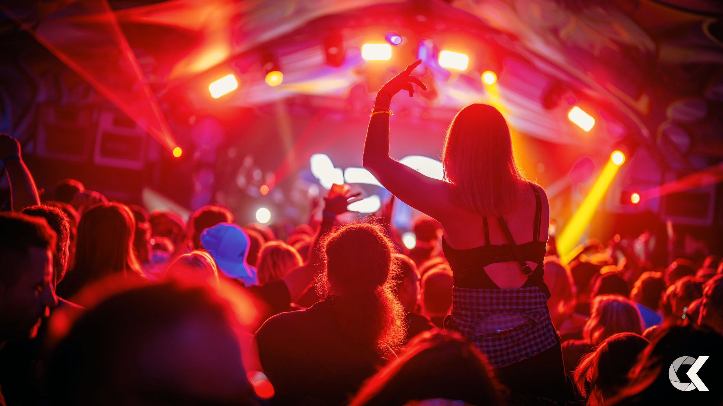 A woman dancing at a concert or music festival with colorful stage lights and a crowd in front of her.