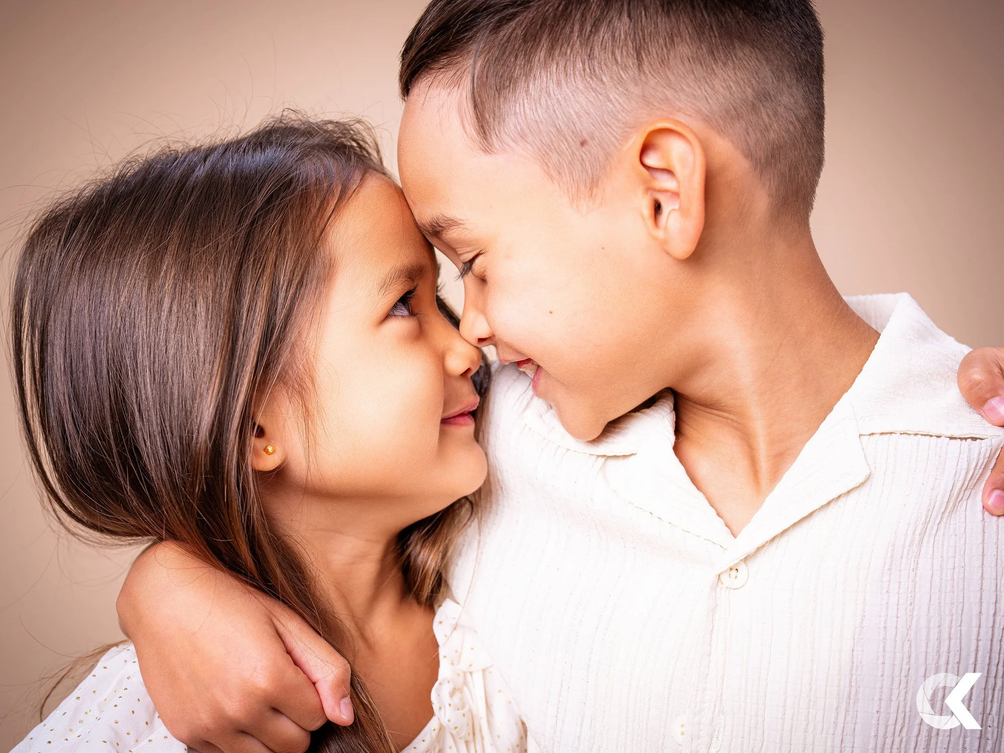 A young girl and a young boy are touching foreheads and smiling, showing affection and closeness.