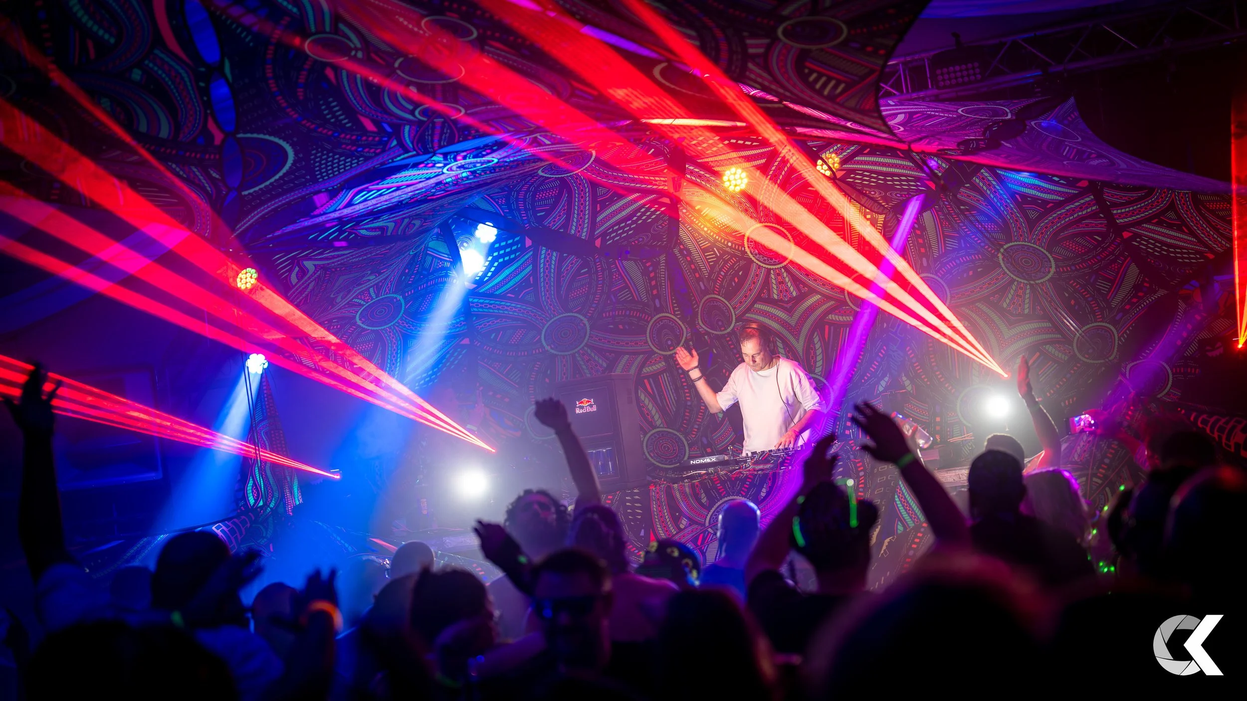 A DJ performing at a nightclub with colorful laser lights and a crowd dancing.