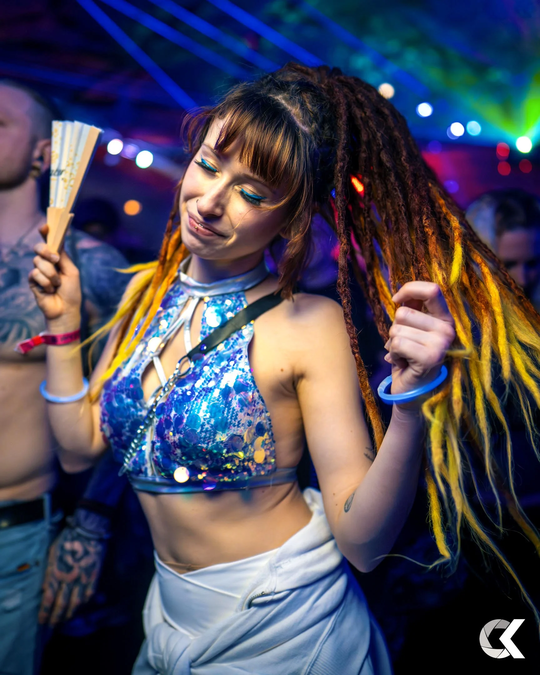 A woman with colorful dreadlocks dancing at a party with vibrant lights in the background.